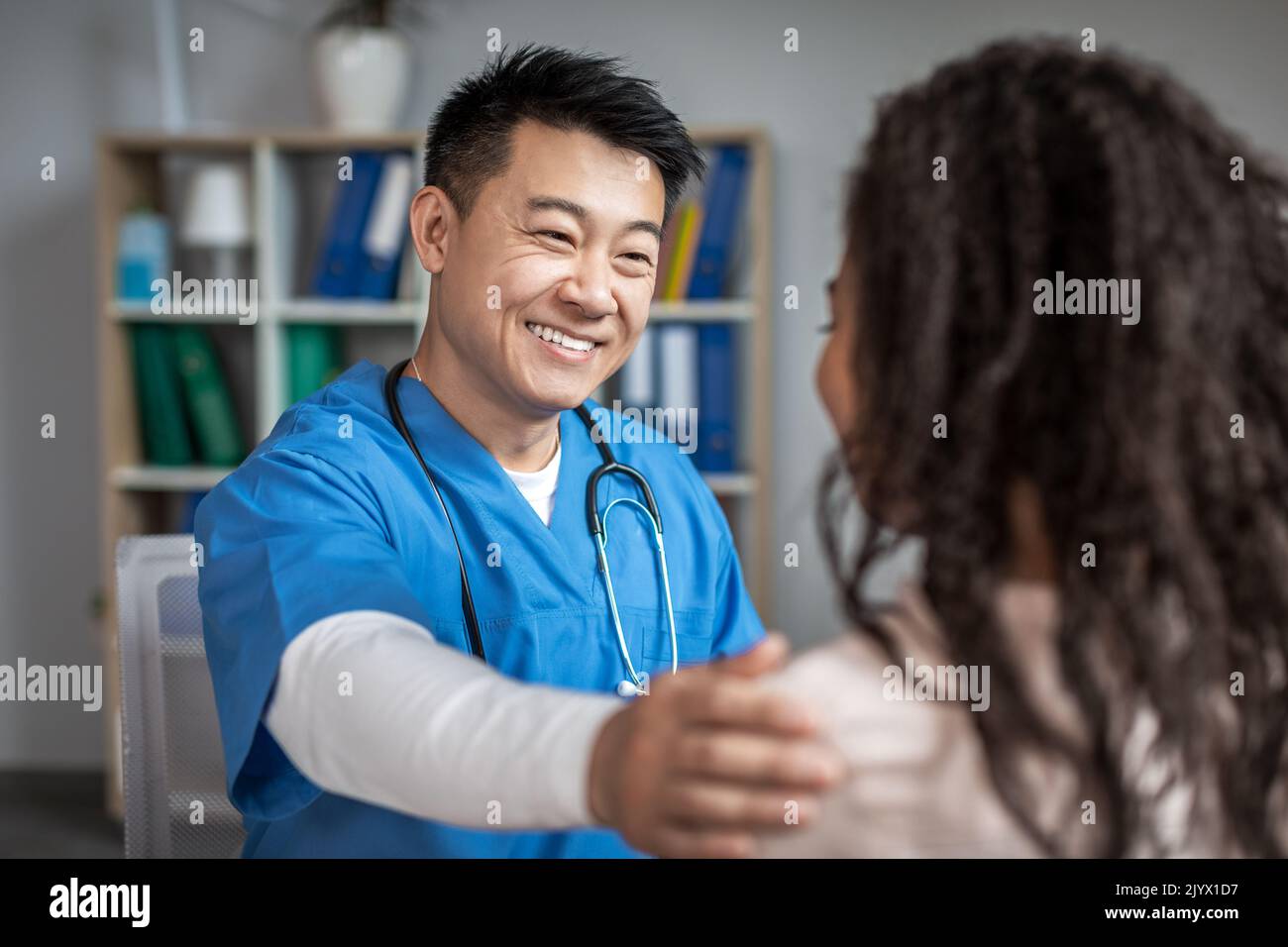 Sorridente medico cinese maschile adulto calma e sostiene giovane afroamericana paziente in clinica Foto Stock