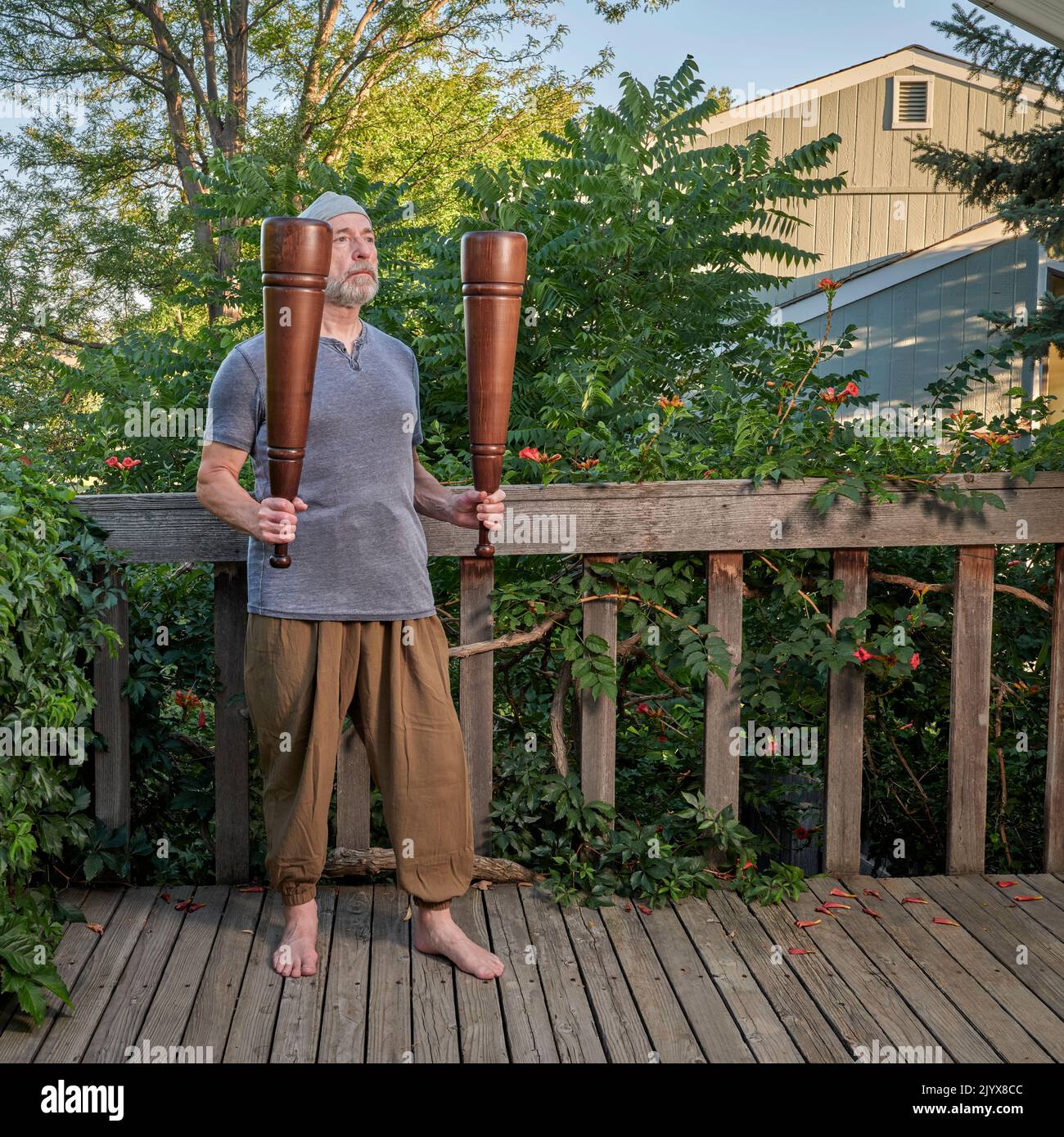 L'uomo anziano (fine 60s) sta esercitandosi con i meels persiani pesanti nel suo patio del cortile posteriore, concetto funzionale di idoneità usando gli attrezzi tradizionali Foto Stock