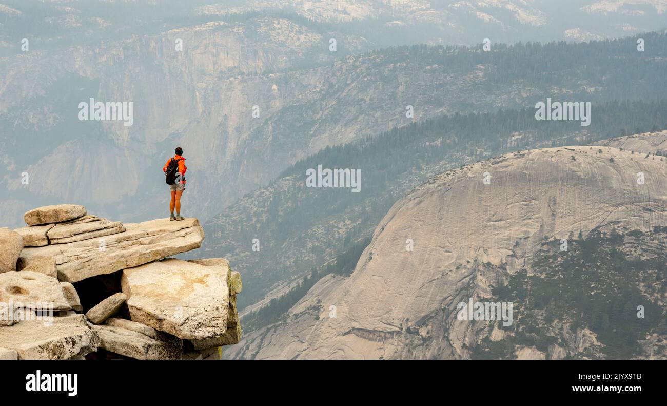 La donna si affaccia sulla Smoky Yosemite Valley sottostante dalla cima della Half Dome Foto Stock