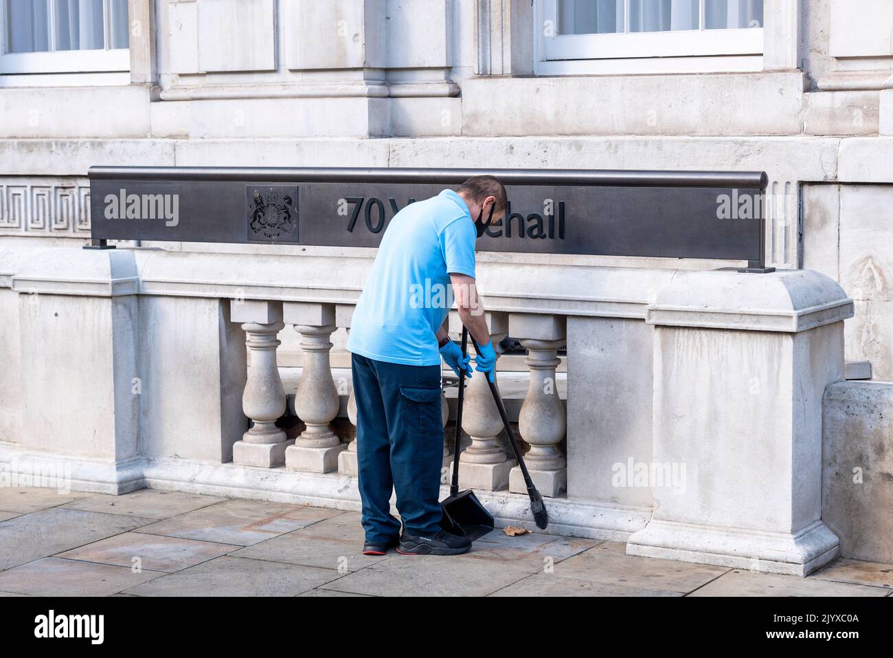 Nuovo concetto di scopa. Lavoratore che spazzano su foglie e mozziconi di sigaretta fuori dal Gabinetto Office, 70 Whitehall, Westminster, Londra, Regno Unito Foto Stock