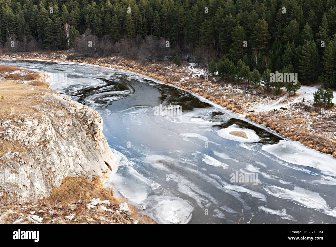 Vista del fiume coperto con le prime scogliere di ghiaccio e neve con erba secca beige e foresta in autunno o inizio inverno Paesaggio tonalità terra Foto Stock