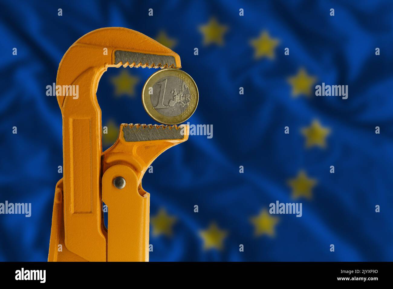 Una moneta in euro contenuta in una chiave per idraulico arancione sullo sfondo della bandiera europea. Lato opposto Foto Stock