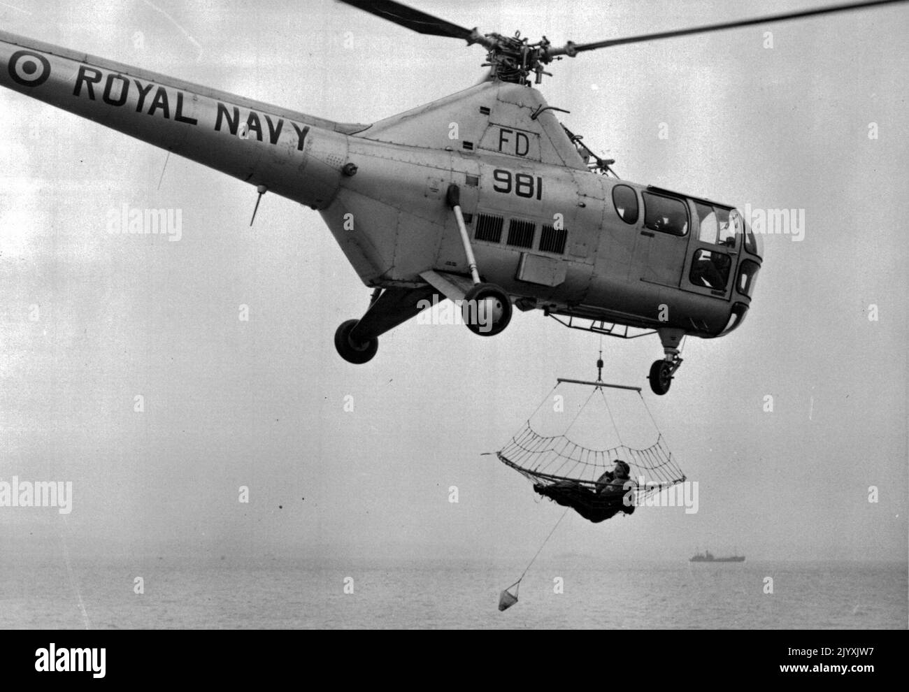 Pesca a strascico per il pesce umano -- Una visione generale della scena sopra il solente questo pomeriggio come Wren 2nd/ufficiale Leta Ridley (Safety Equipment Officer) viene trasportato fino all'elicottero dopo essere stato 'pescato' dal mare durante la dimostrazione del nuovo apparecchio. All'altezza della R.N. Air Station Gosport (Hants) oggi è stata presentata una dimostrazione del nuovo apparato elicottero per il salvataggio delle vittime dal mare, sviluppato dall'unità di ricerca e salvataggio della R.N. Air Station, Ford, Sussex, il nuovo apparecchio è come un'enorme rete da traino per 'pescare' sopravvissuti dal mare. Gennaio 24, 1955. (Foto di F Foto Stock