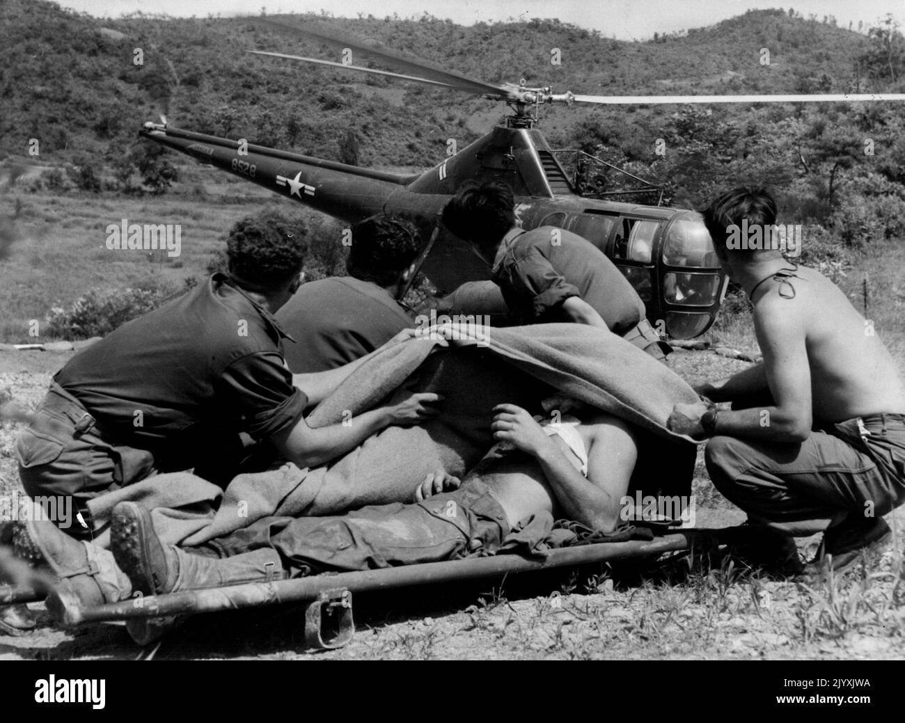 Un fattore tremendo nel risparmio di ***** Vive in Corea è il lavoro svolto da Air Evacuation Helicopters - 'choppers' per le truppe. Qui la vittima è pte Alan Brown South Australia ***** ferito nel collo da frammenti di mortaio. Gli ordini medici lo proteggono con i loro corpi e una coperta, dal vento alto creato dalle palette del rotore 'choppers' come viene a terra. Luglio 15, 1953. Foto Stock