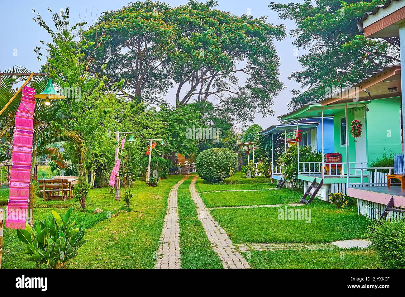Il vicolo in mezzo al parco tropicale verde con linea di piccole case turistiche, Pai, Thailandia Foto Stock