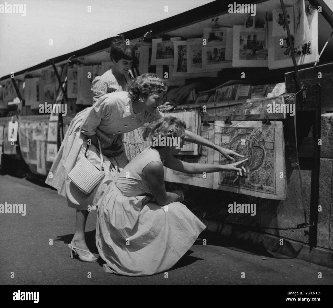 Vecchie mappe e stampe colorate, acquerelli originali e oli di artisti della Rive Gauche, sono venduti a basso costo nelle piccole bancarelle lungo la Senna vicino a Nortre Dame. Fay Muller e Beryl Penrose individuano la loro posizione su un'antica mappa. Giugno 21, 1955. (Foto di Michael Brodsky). Foto Stock