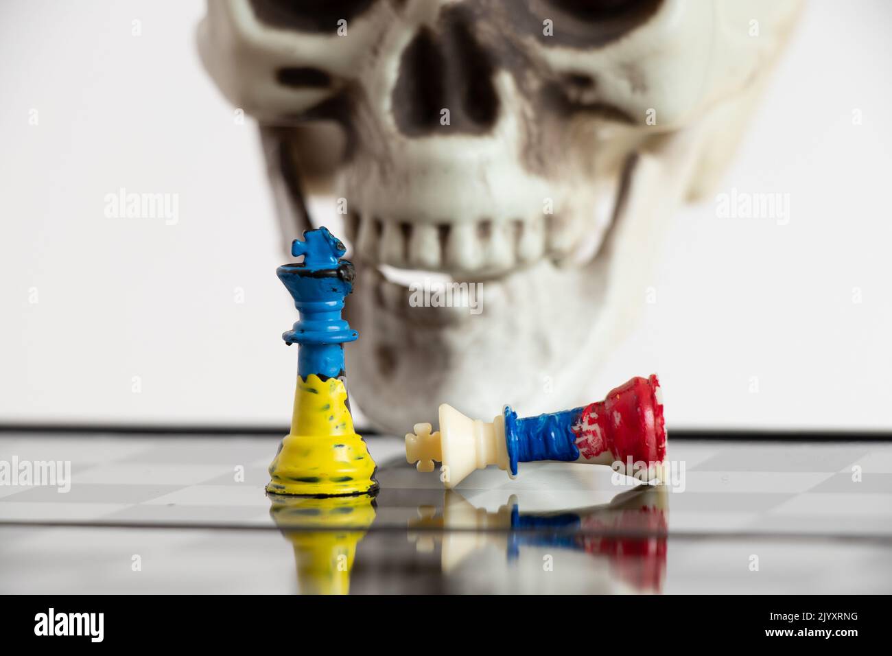 Scacchi con una bandiera dipinta di Russia e Ucraina su una scacchiera e una testa di uno scheletro sullo sfondo, una partita di morte tra i due paesi di Foto Stock