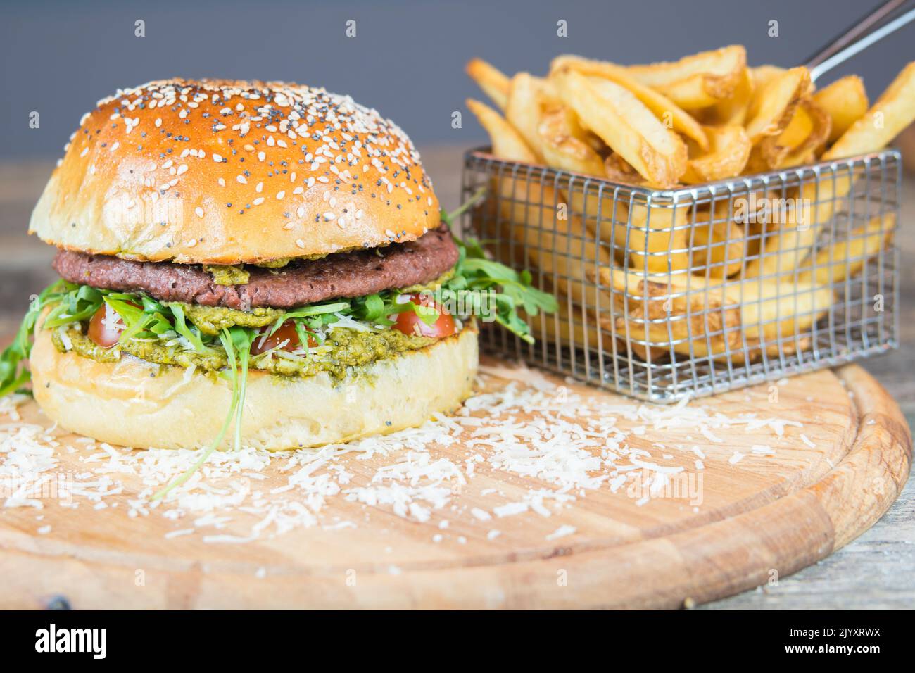 Menu di hamburger vegani con patatine fritte sul banco di taglio in legno. Hamburger con formaggio vegano, pesto e sostituto di carne, rucola, pomodori ciliegini. Foto Stock