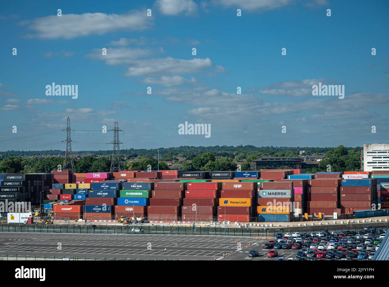 Southampton, Inghilterra, Regno Unito - 7 luglio 2022: Panorama del porto. Banchina con contenitori impilati di tutte le origini. Parcheggio auto di fronte sotto il paesaggio blu e g Foto Stock