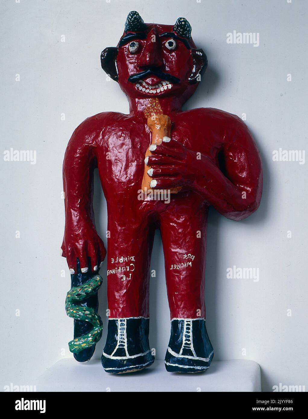 Fotografia a colori di una scultura del 3D di una figura diabolica che tiene una pentola in una mano e un oggetto intrecciato da un serpente nell'altra mano. Foto Stock