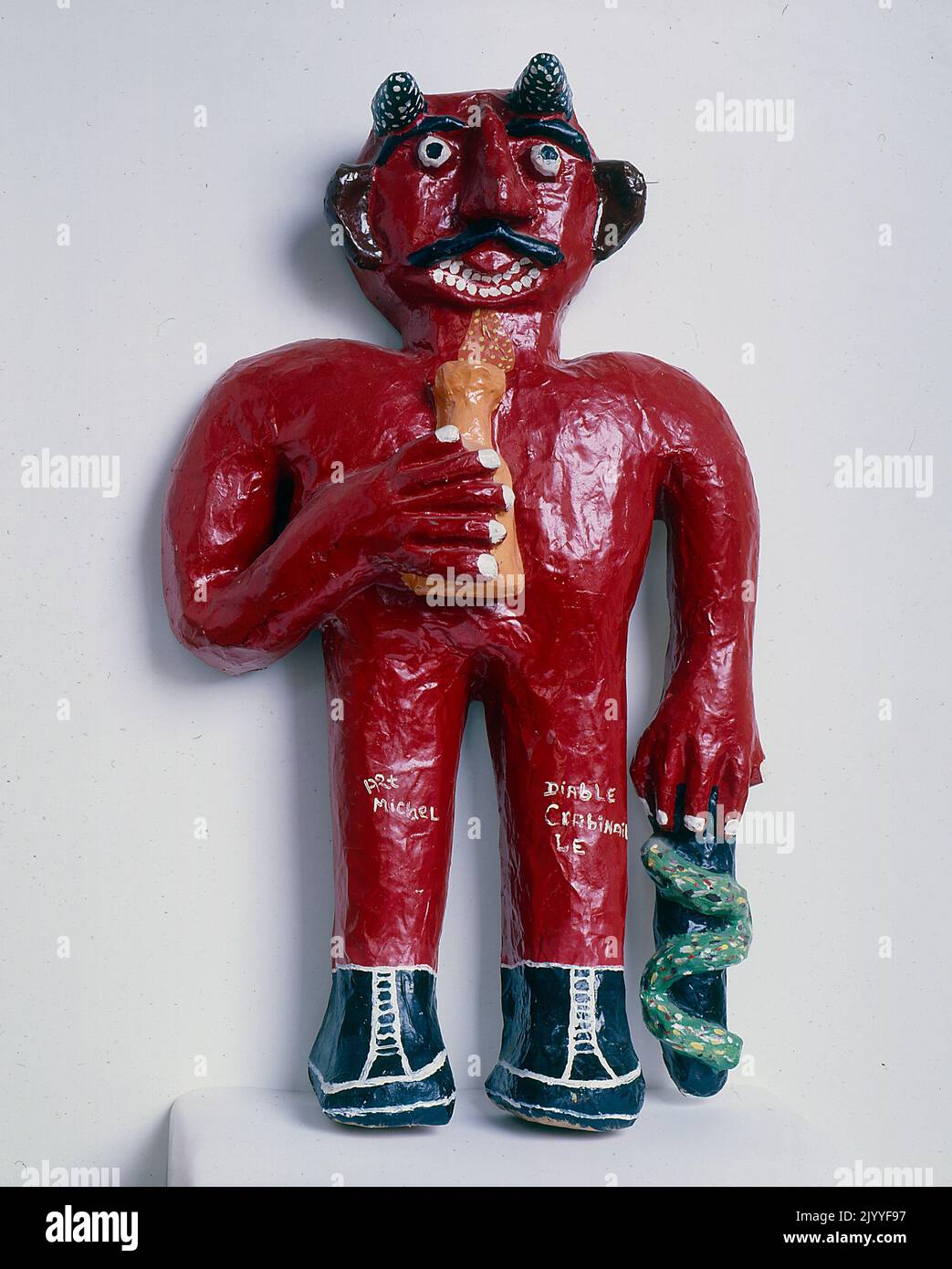 Fotografia a colori di una scultura del 3D di una figura diabolica che tiene una pentola in una mano e un oggetto intrecciato da un serpente nell'altra mano. Foto Stock