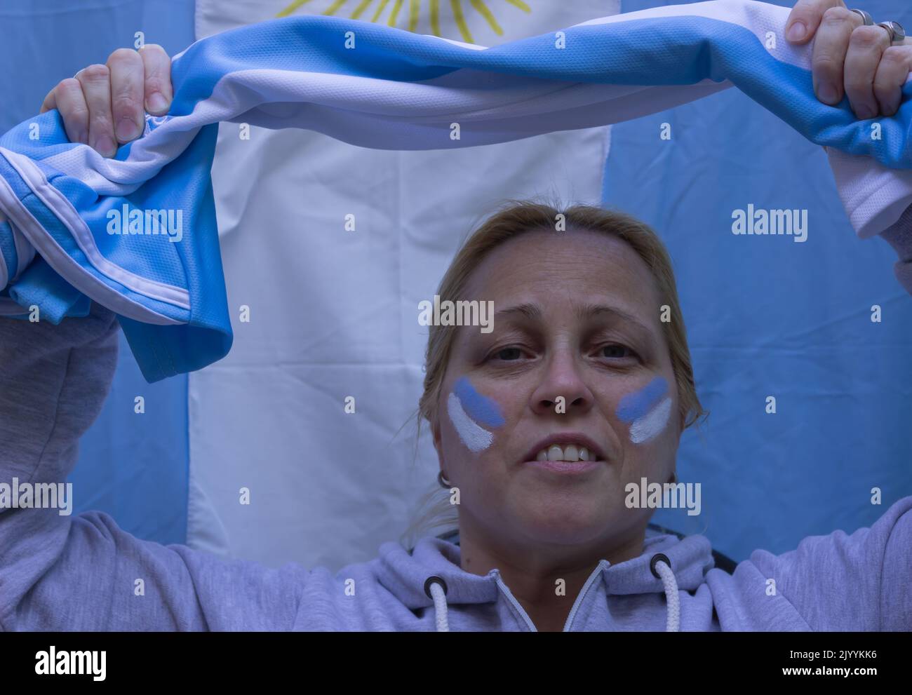 Donna bionda con una bandiera e volto dipinto nei colori dell'Argentina guardando una partita di calcio. Foto Stock