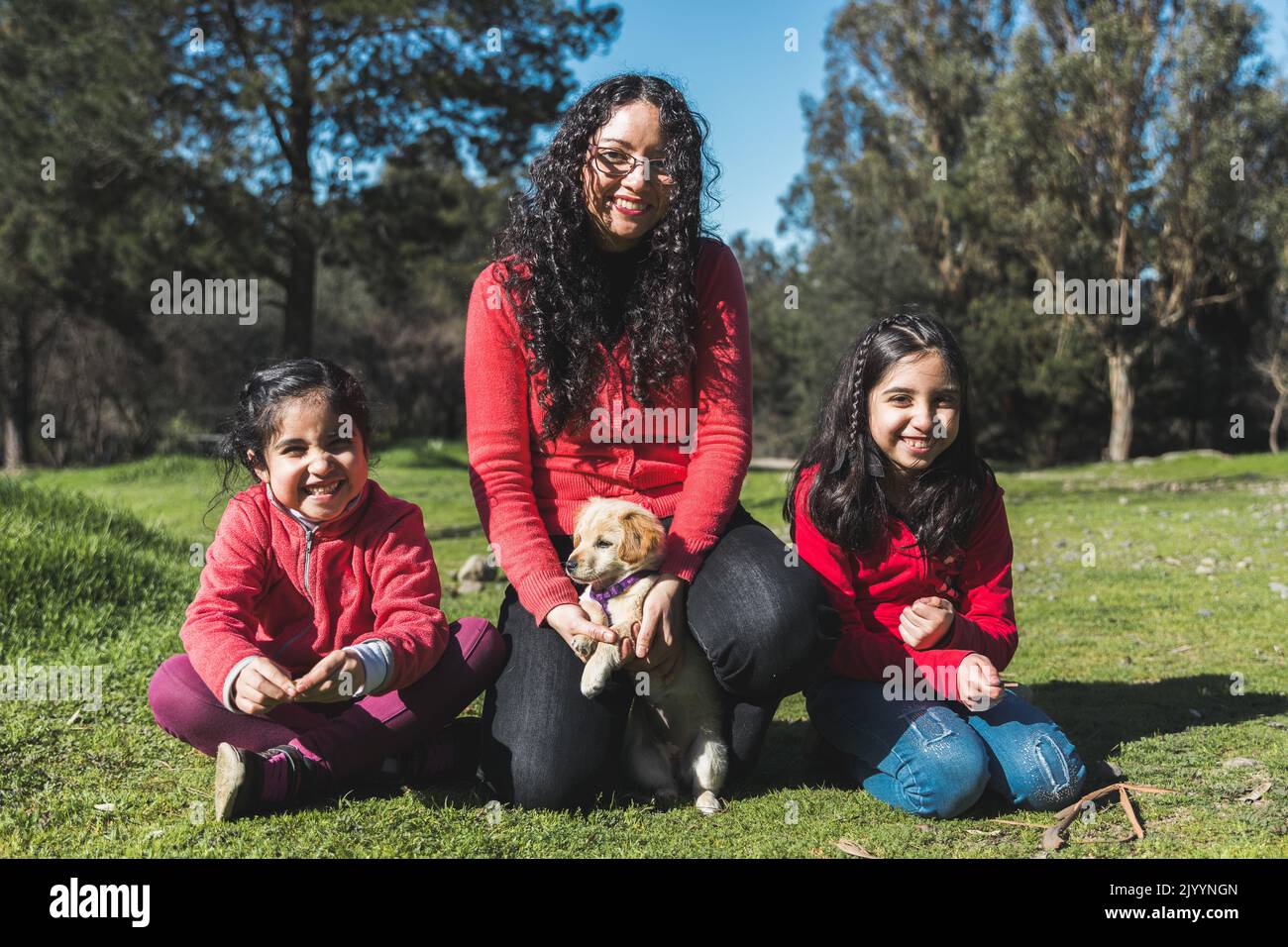 Giovane donna con le sue due figlie sull'erba e giocando con un cucciolo di recupero d'oro nel parco Foto Stock