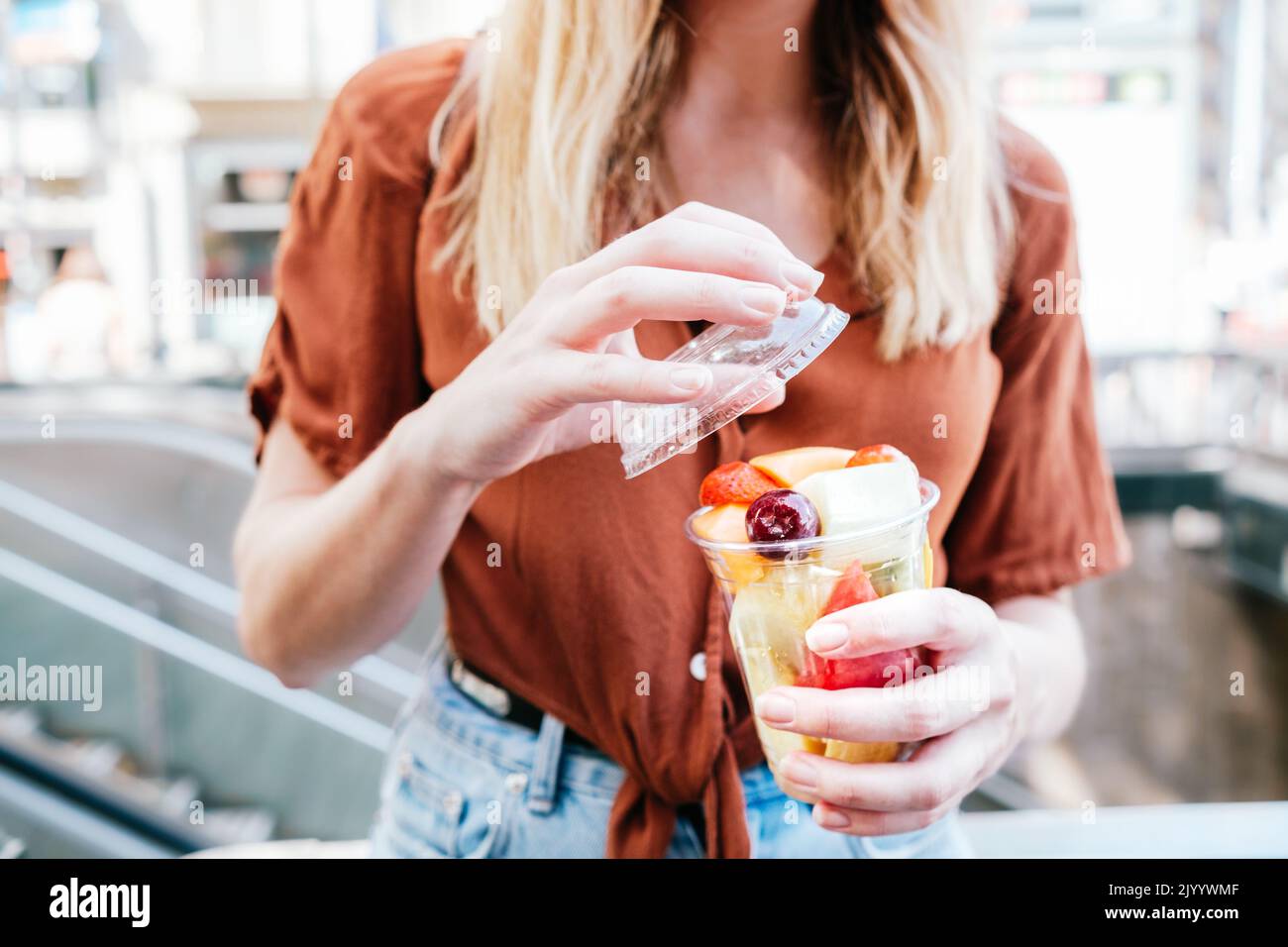 ragazza turista irriconoscibile che apre una tazza di frutta fresca affettata. È per strada Foto Stock
