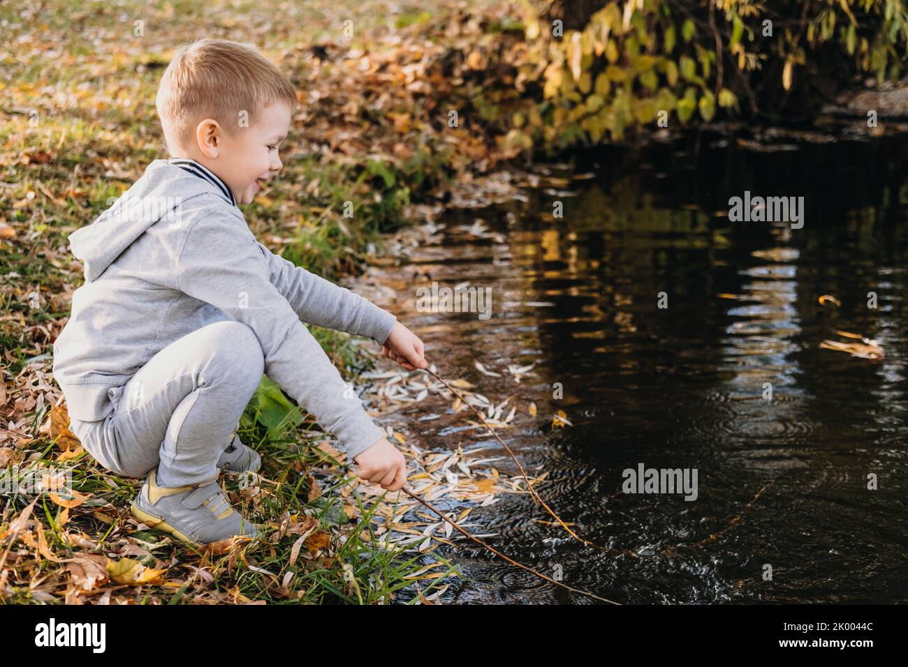Ragazzo carino che gioca al bordo di un ruscello guardando l'acqua in una primavera nuvolosa o in un giorno di autunno. Tempo libero nella foresta in giornata di sole felice famiglia Foto Stock