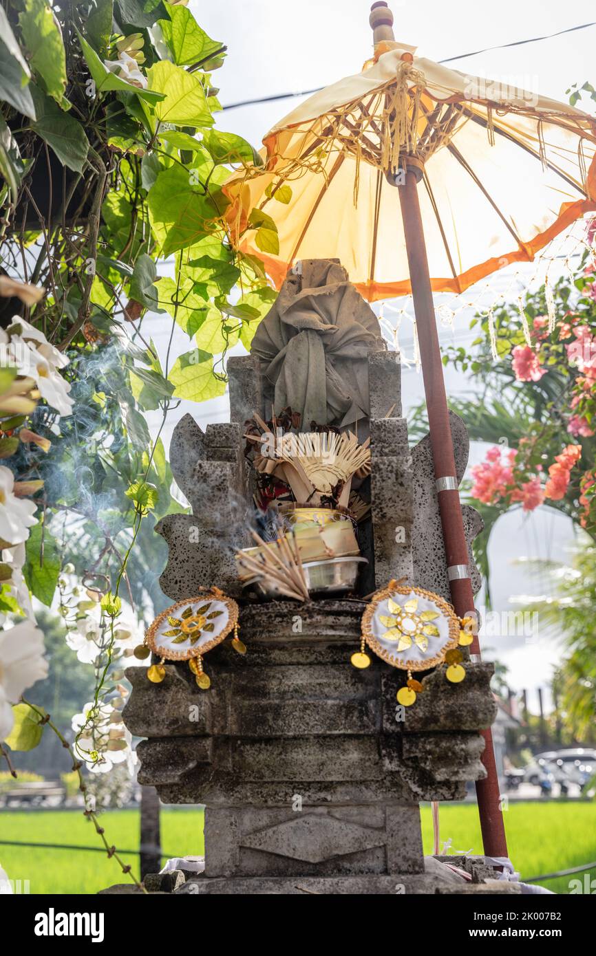 Altare indù balinese con ombrello giallo, offerte e incenso ardente. Bali, Indonesia, Foto Stock