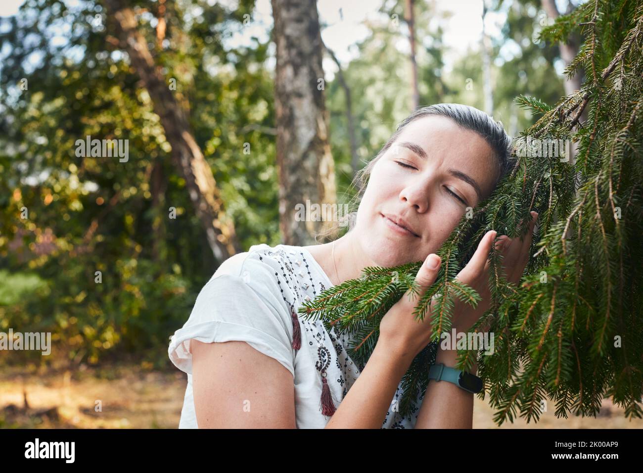 Una donna abbraccia un albero di conifere nella foresta. Il concetto di vivere in prossimità della natura e della foresta. Vista frontale. Foto Stock