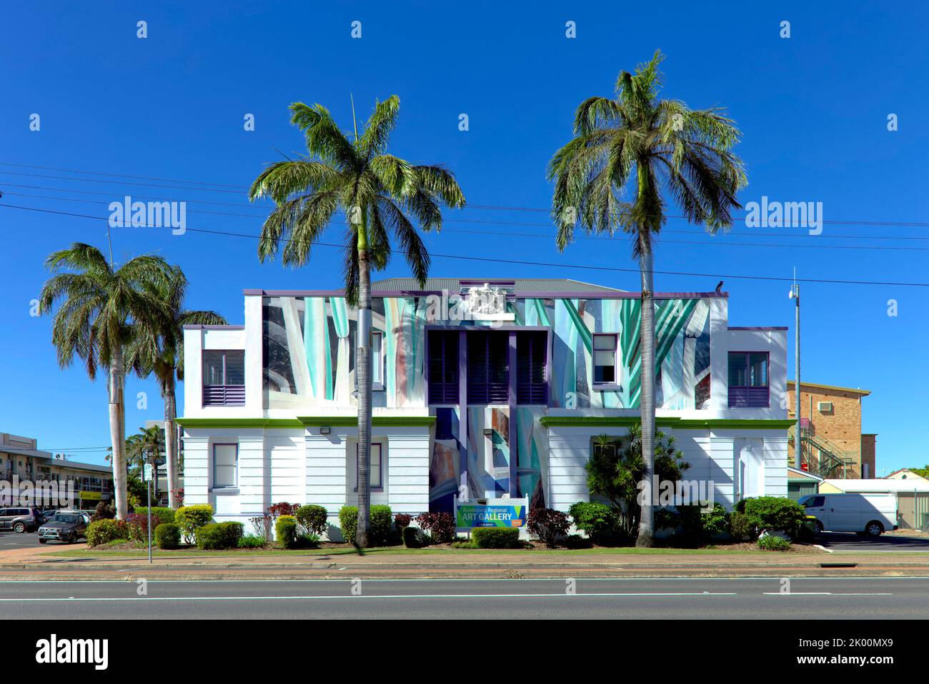 Edificio architettonico moderno con finestre riflettenti e design esterno tra palme tropicali sotto il cielo azzurro Foto Stock