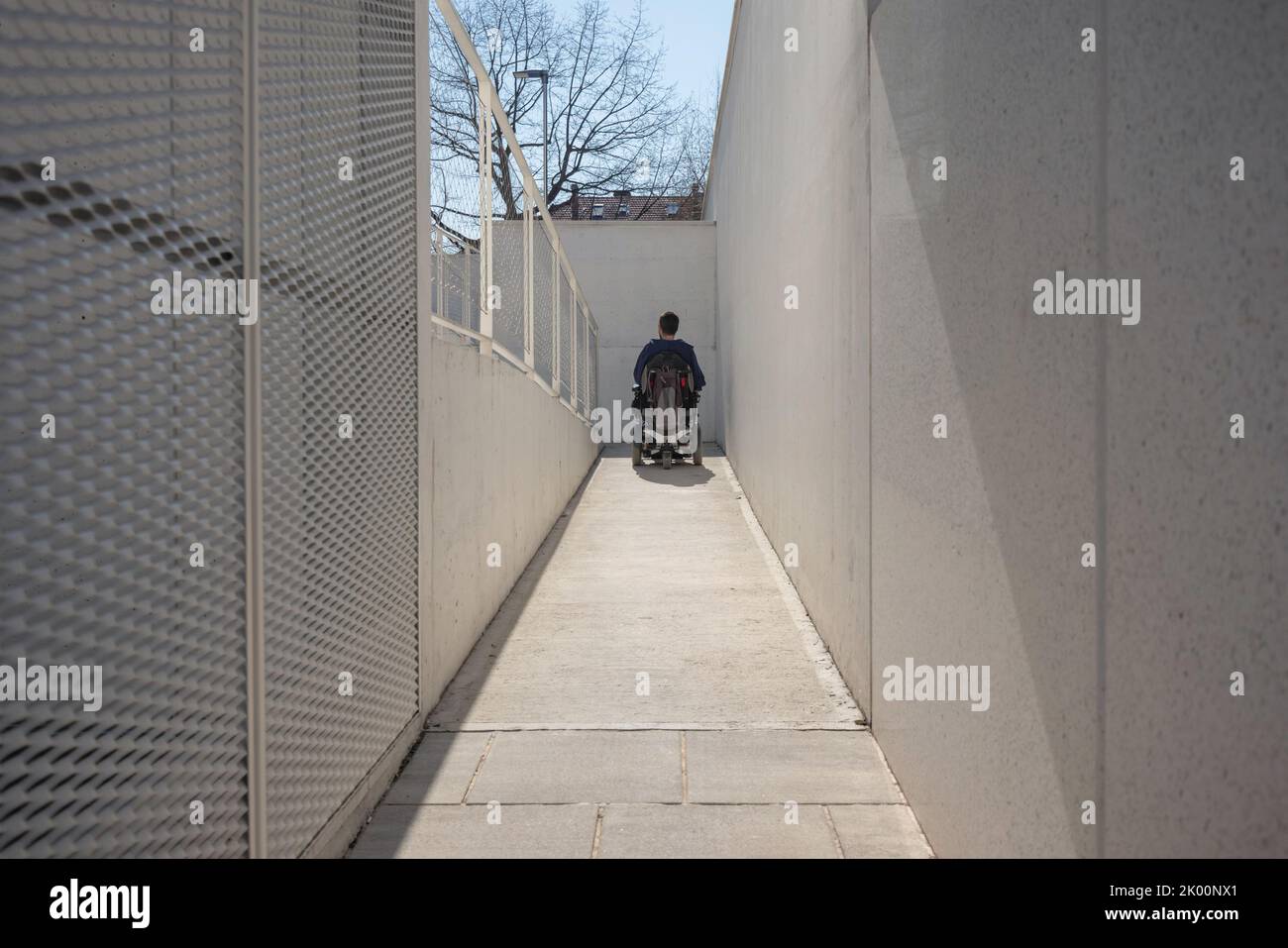 Uomo su sedia a rotelle, in avvicinamento all'edificio che si sposta lungo una rampa accessibile per persone con disabilità Foto Stock