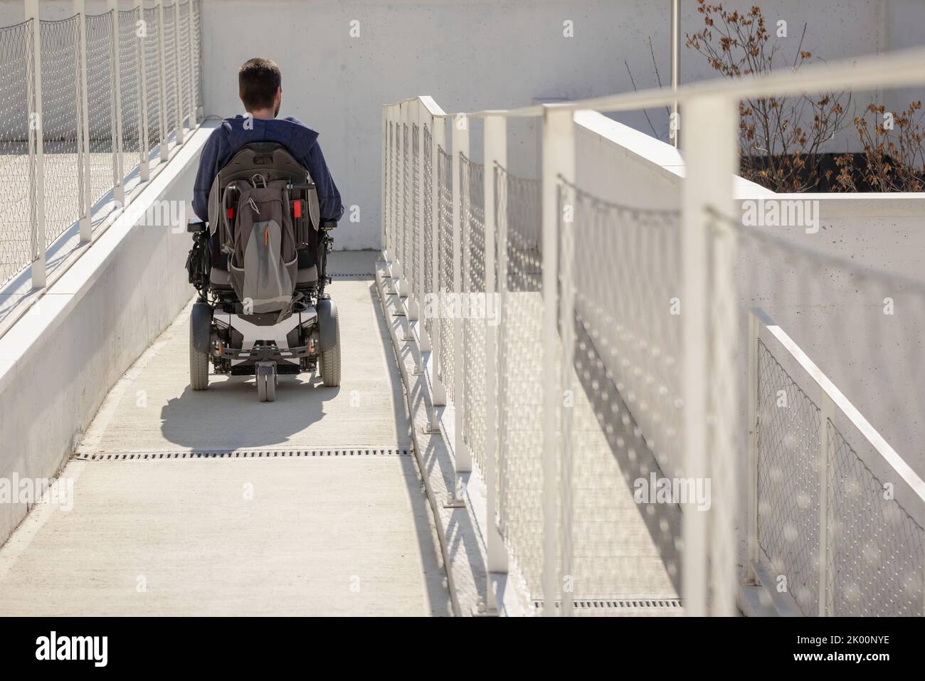 Uomo su sedia a rotelle, in avvicinamento all'edificio che si sposta lungo una rampa accessibile per persone con disabilità Foto Stock