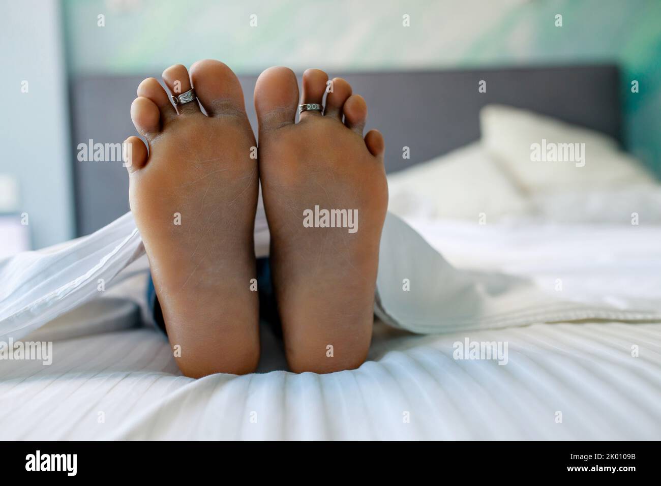Primo piano dei piedi femminili nel letto in camera da letto sotto coperta Foto Stock