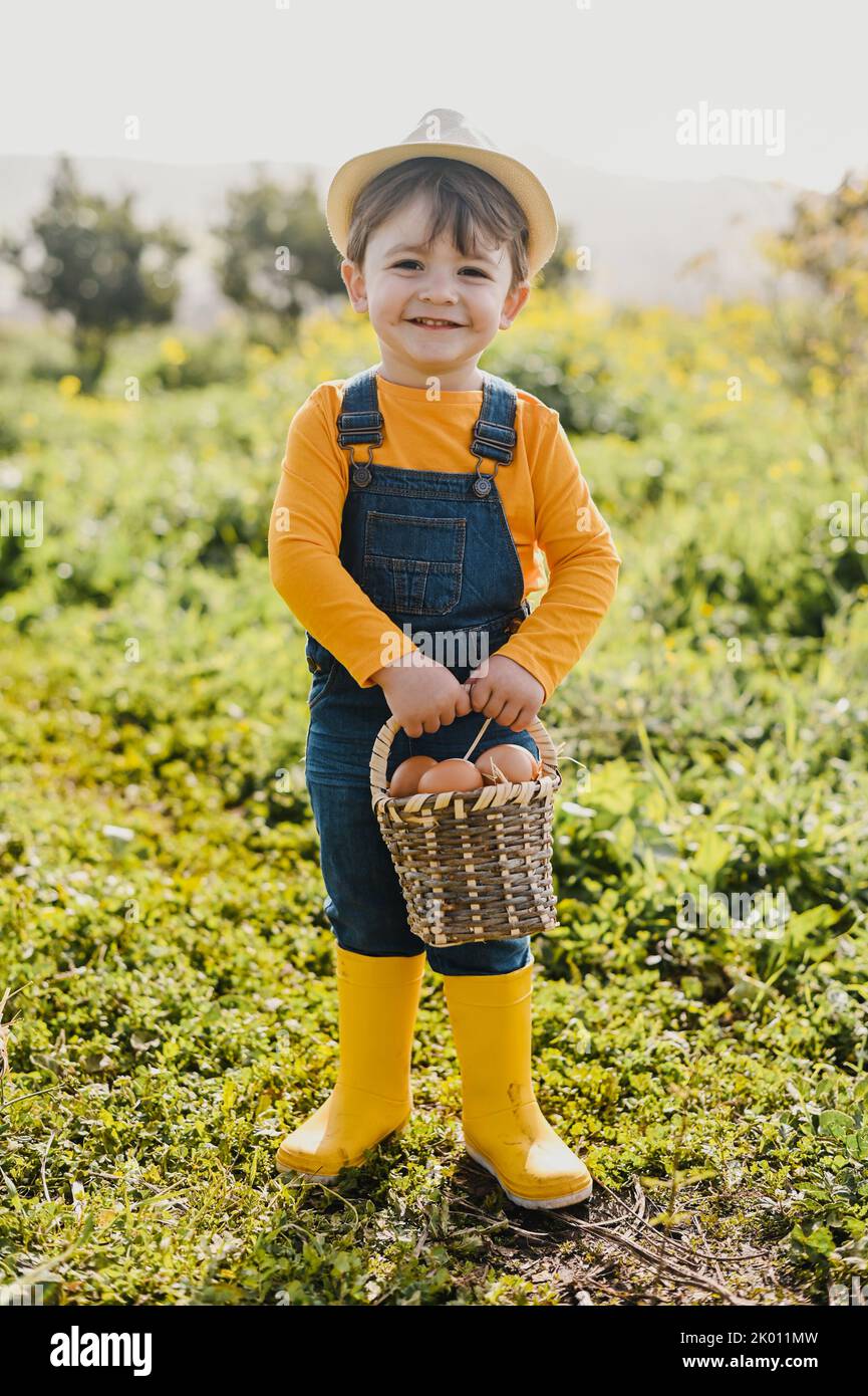 Carino ragazzo felice con cestino di uova sorridente in fattoria alla luce del sole Foto Stock