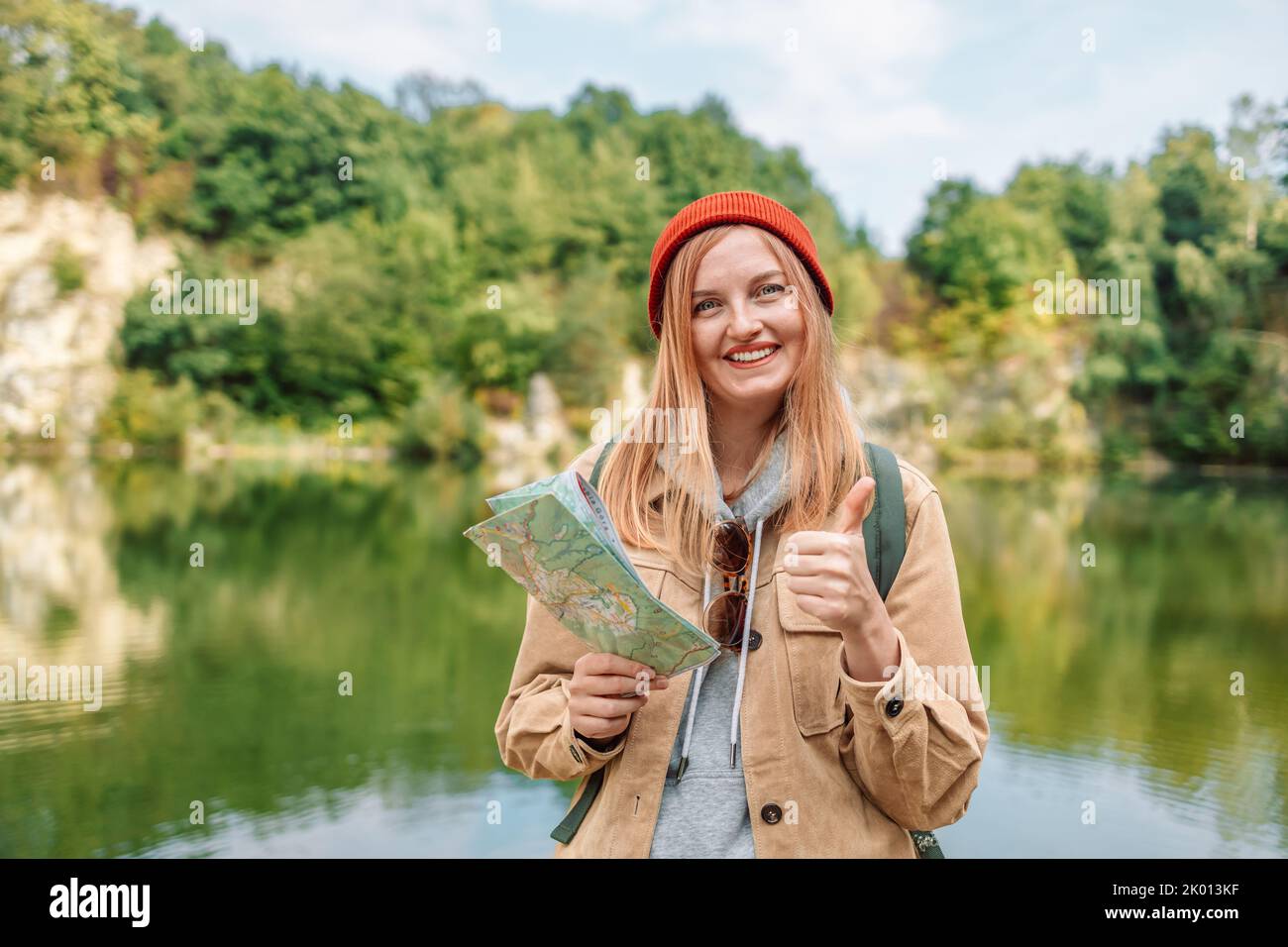 Una donna felice in viaggio con spettacoli come lo zaino, guardando la fotocamera e la mappa topografica nelle foreste verdi. Avventura escursionistica vacanza estiva concetto. Foto Stock