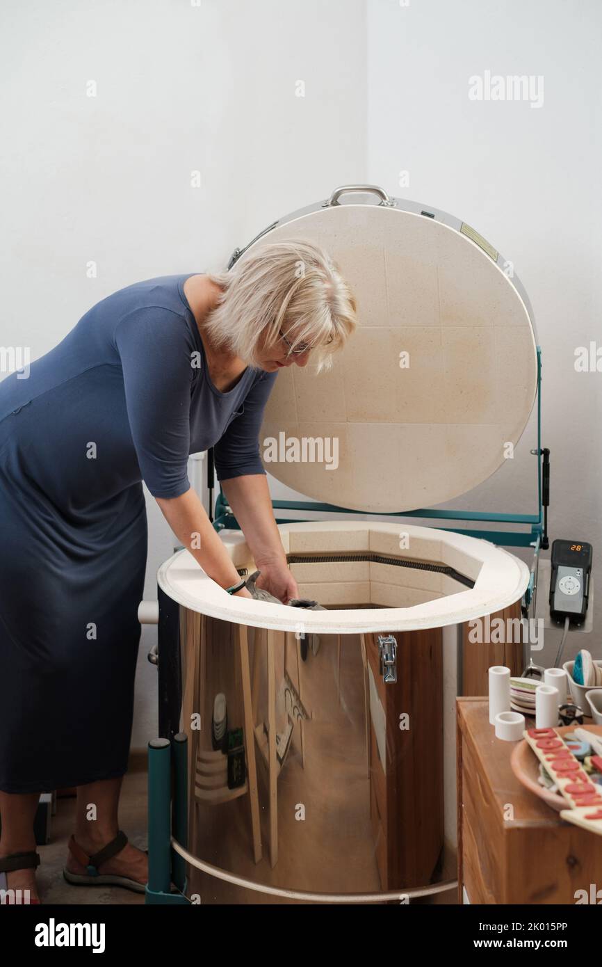 Donna artista mettere ceramica in forno. Ceramica cruda pronta per essere cotta in forno. Ceramista che lavora in studio per la realizzazione di vasi e piatti. Modellazione di argilla Foto Stock