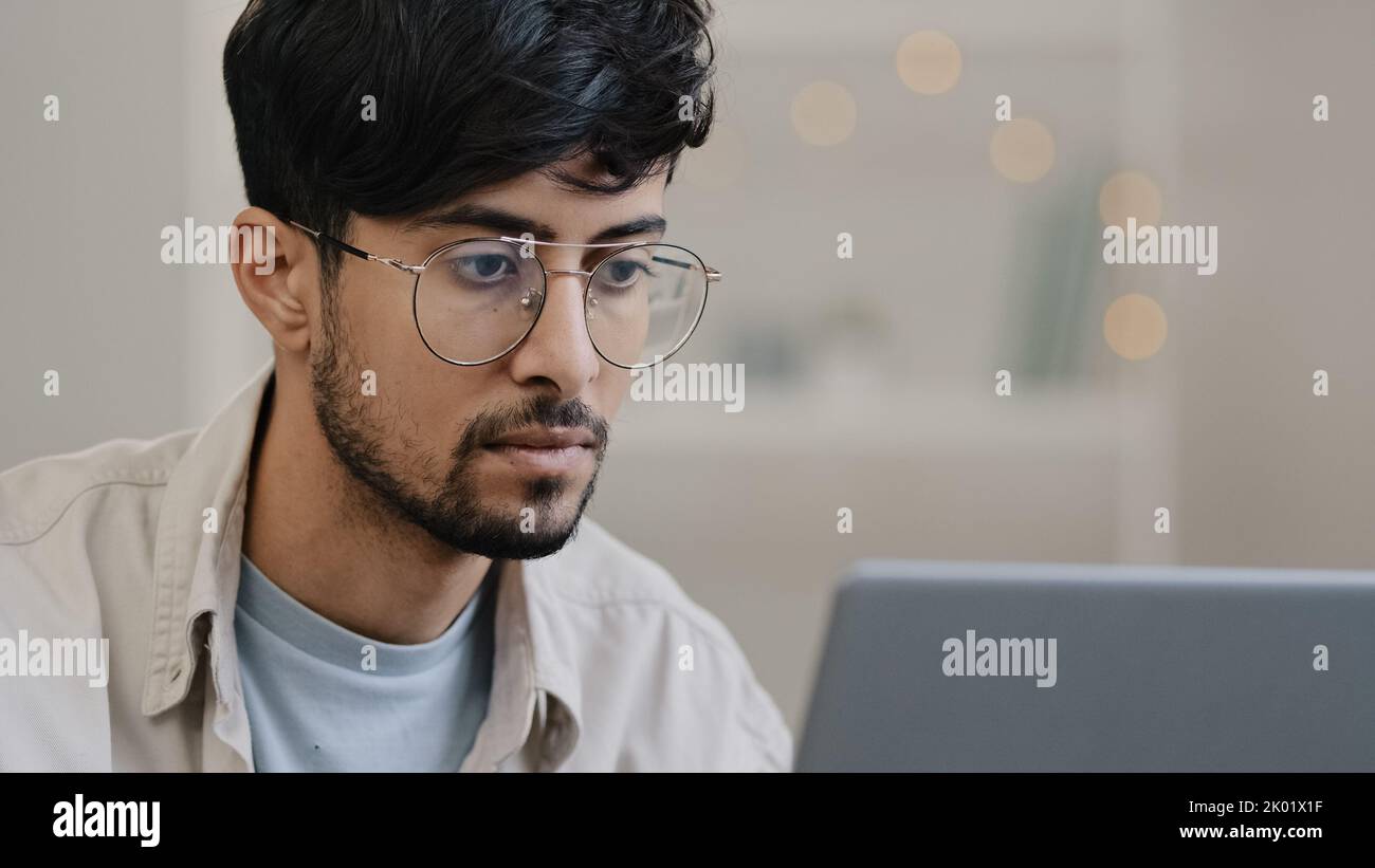 Primo piano maschio faccia arabo uomo ispanico barbuto ragazzo che lavora con il notebook sente stress sofferenza di mal di testa toglie gli occhiali sfrega gli occhi preoccupati Foto Stock