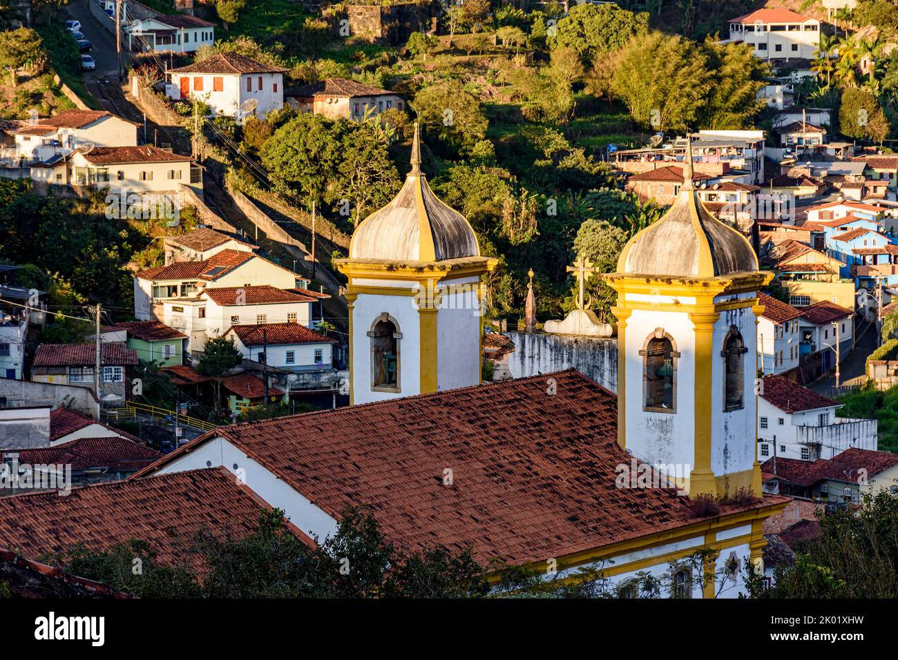 Torri e campane di un'antica chiesa barocca con le case della città di Ouro Preto sullo sfondo Foto Stock