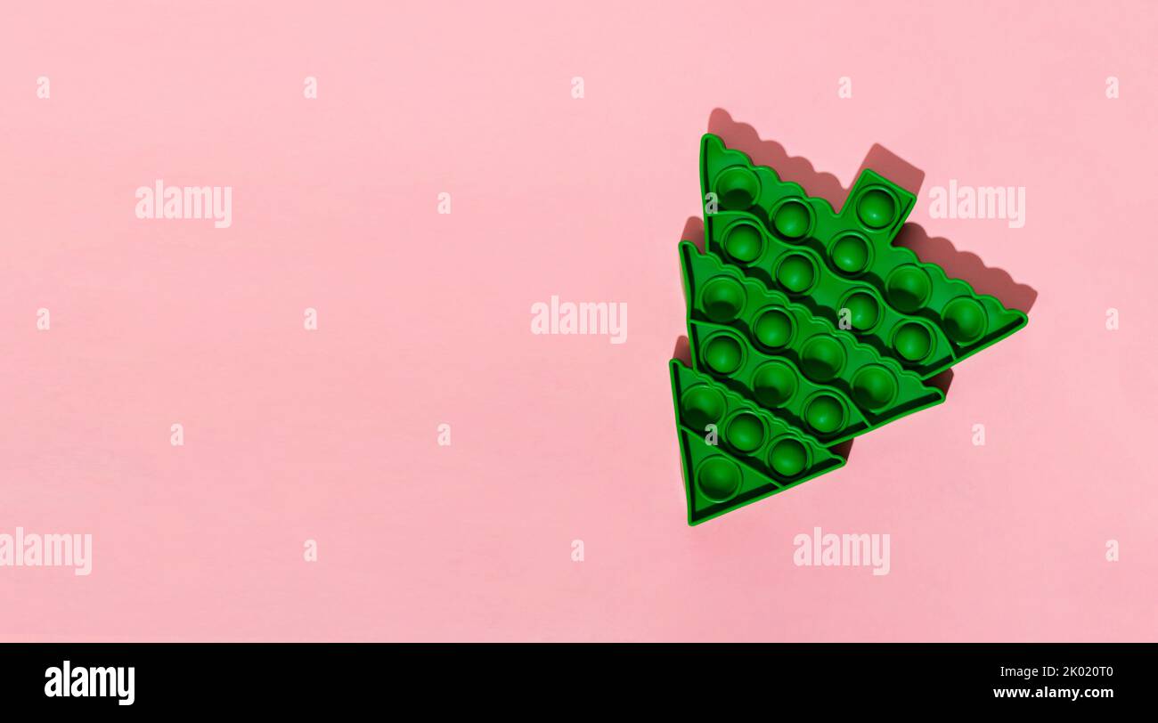 Un trendy popolare capretti anti lo schiocco di sforzo esso giocattolo sotto forma di albero verde di Natale che cade giù sullo sfondo rosa pastello. Vacanza concetto minimo di Natale Foto Stock