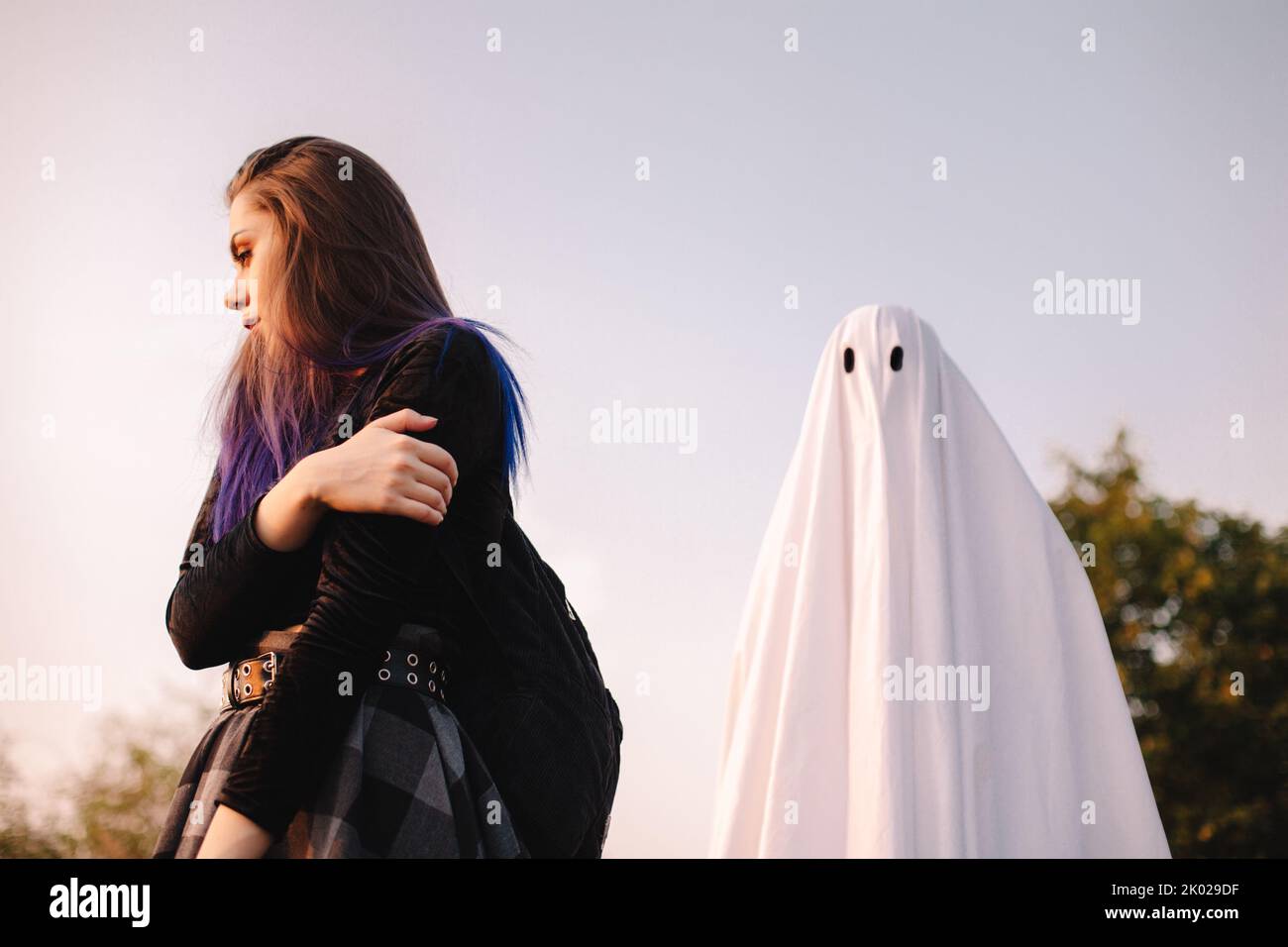 Fantasma in piedi dietro la giovane donna spaventata all'aperto durante Halloween Foto Stock