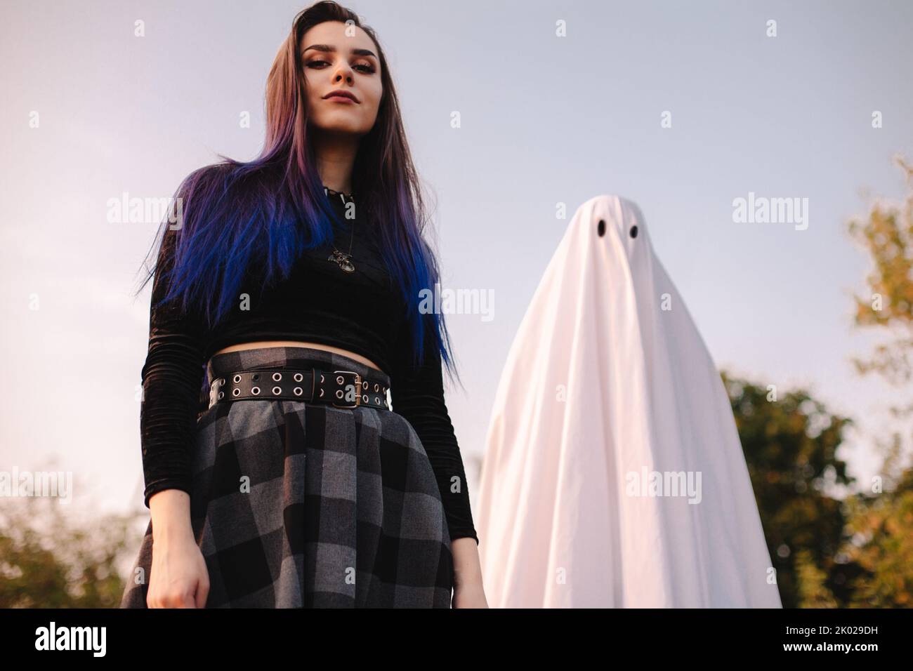 Felice giovane donna in piedi con fantasma contro il cielo blu all'aperto durante Halloween Foto Stock