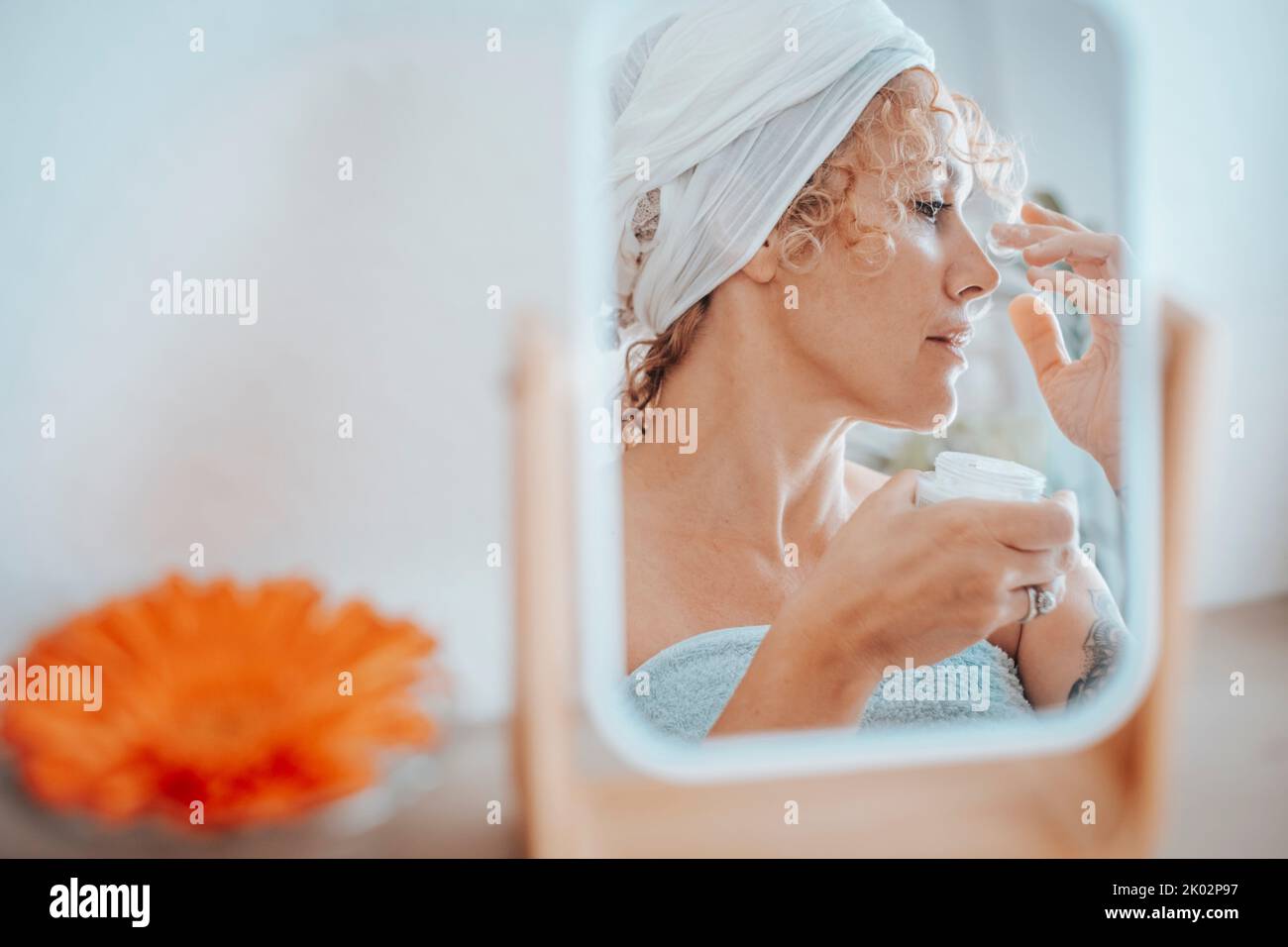 Bella giovane donna adulta che si cura della sua pelle a casa. Donna riflessa in uno specchio nella bellezza attività di svago. Cura della pelle e creme per prodotti di invecchiamento. Persone che utilizzano pelle cosmetica naturale Foto Stock