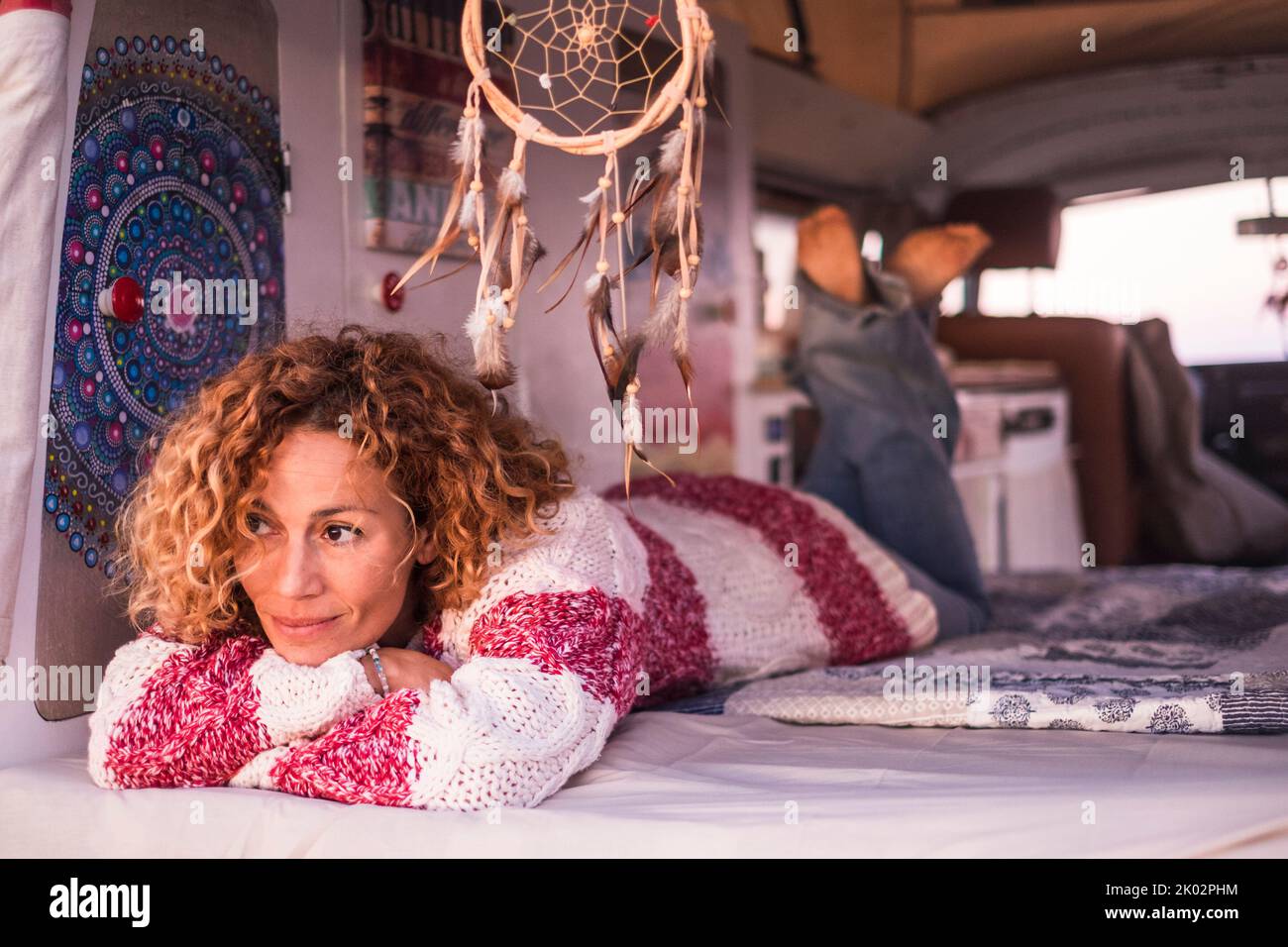 Bella donna adulta caucasica si adagia all'interno di un vecchio furgone classico restaurato casa fatta. Viaggi hippy vanlife persone che ammirano all'aperto. Donna moderna che ha tempo di relax in camera da letto camper bus Foto Stock