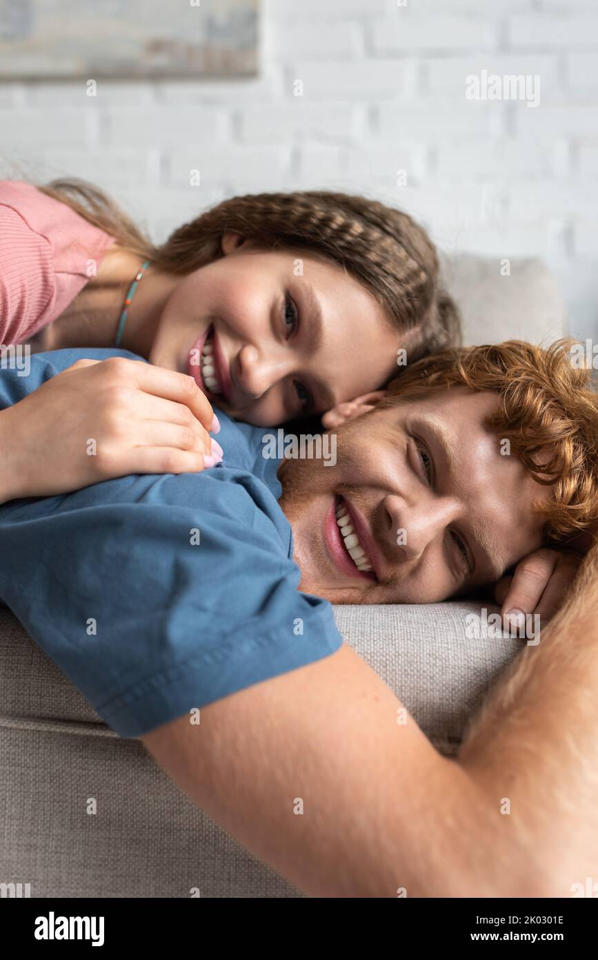 ragazza giovane gioiosa sdraiata sul retro del ragazzo sorridente e riposante sul divano, immagine stock Foto Stock
