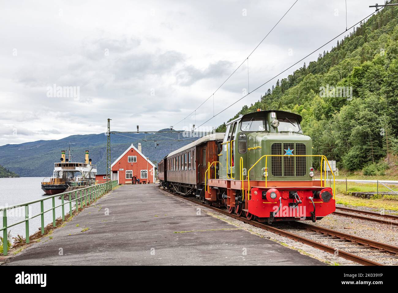 Norvegia, Vestfold og Telemark, Rjukan, Mæl, stazione ferroviaria, treno in piedi sulla piattaforma, locomotiva diesel, carrozze in legno di teak, traghetto a vapore ammoniaca (sfondo) Foto Stock