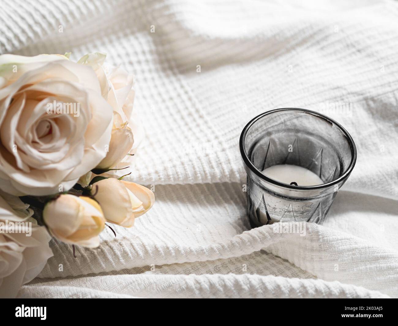 Una candela su una tazza con una rosa bianca su un panno bianco Foto Stock