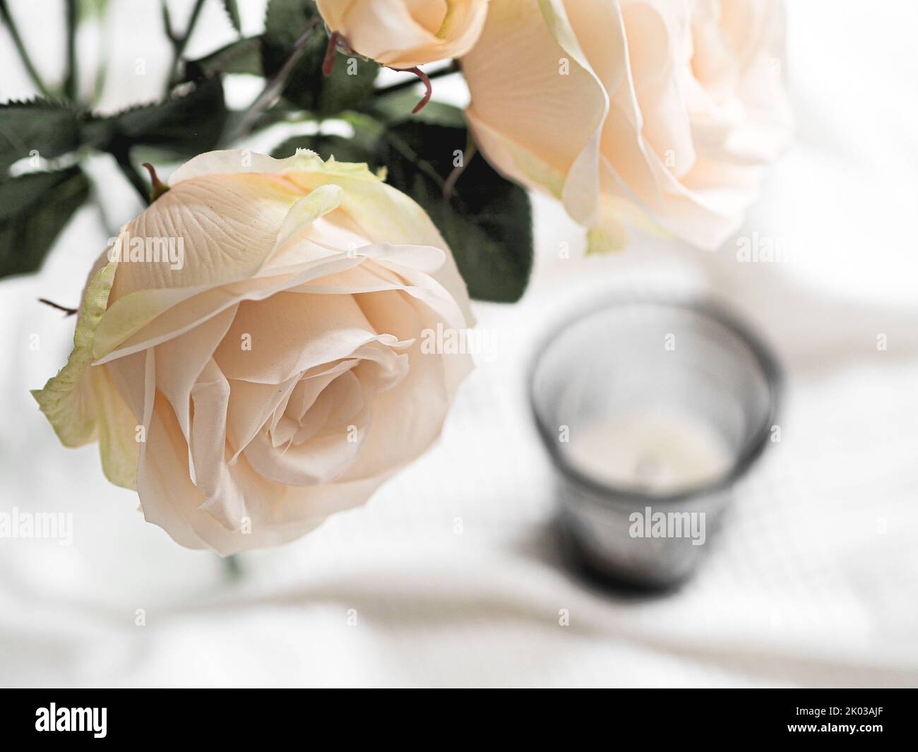 Una candela su una tazza con una rosa bianca su un panno bianco Foto Stock