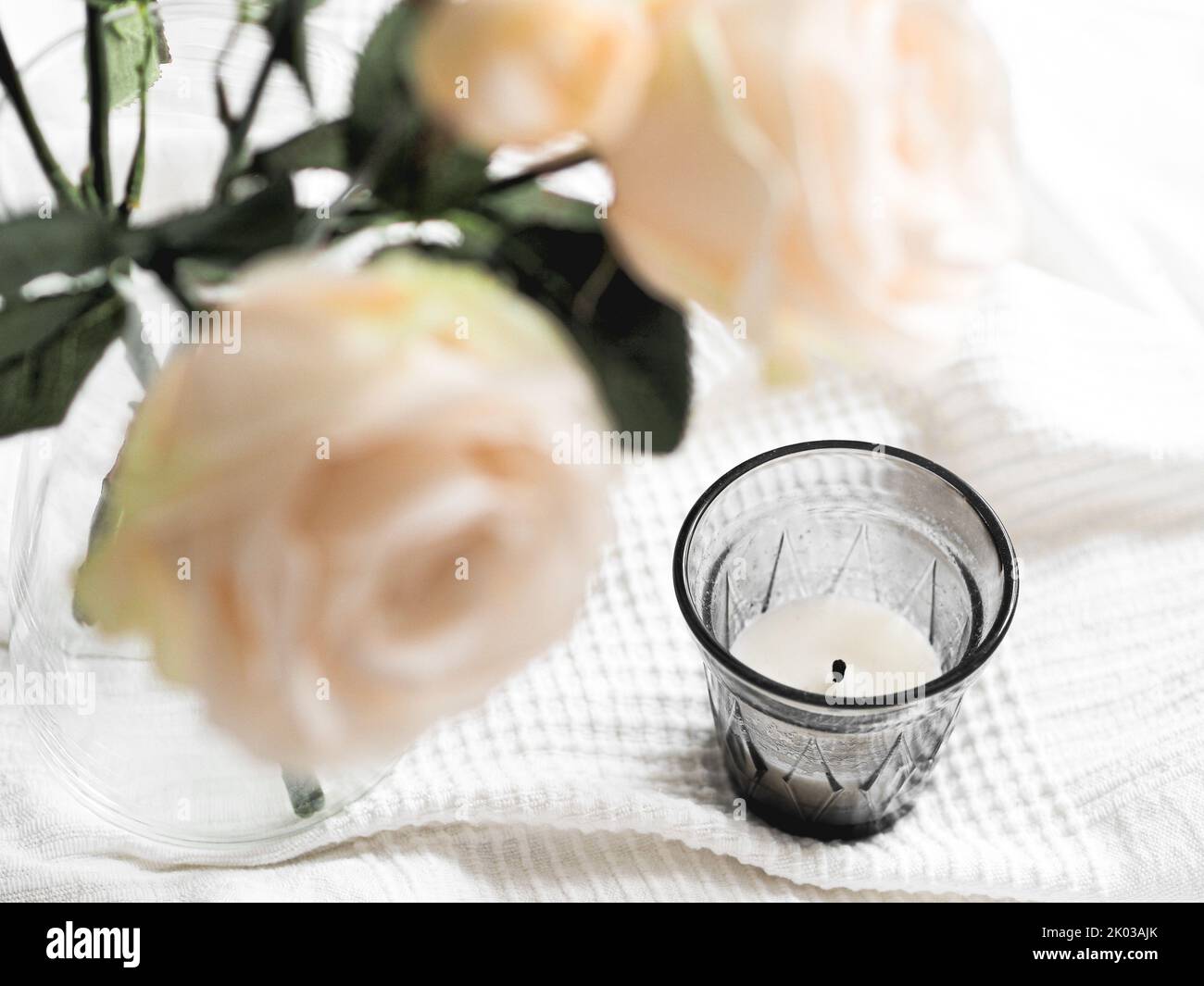 Una candela su una tazza con una rosa bianca su un panno bianco Foto Stock