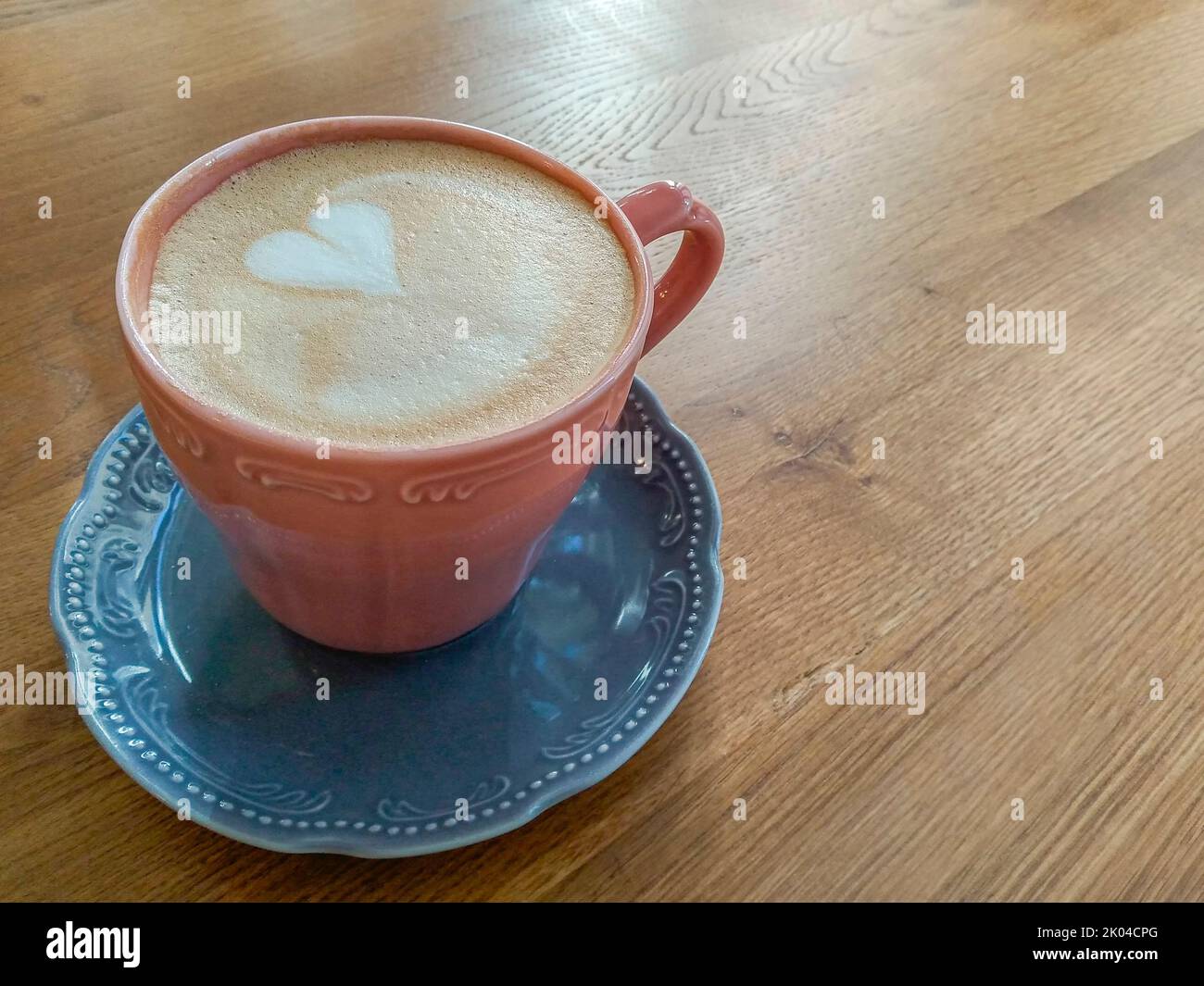 tazza di caffè rosso sul piattino blu con latte a forma di cuore sul tavolo di legno Foto Stock