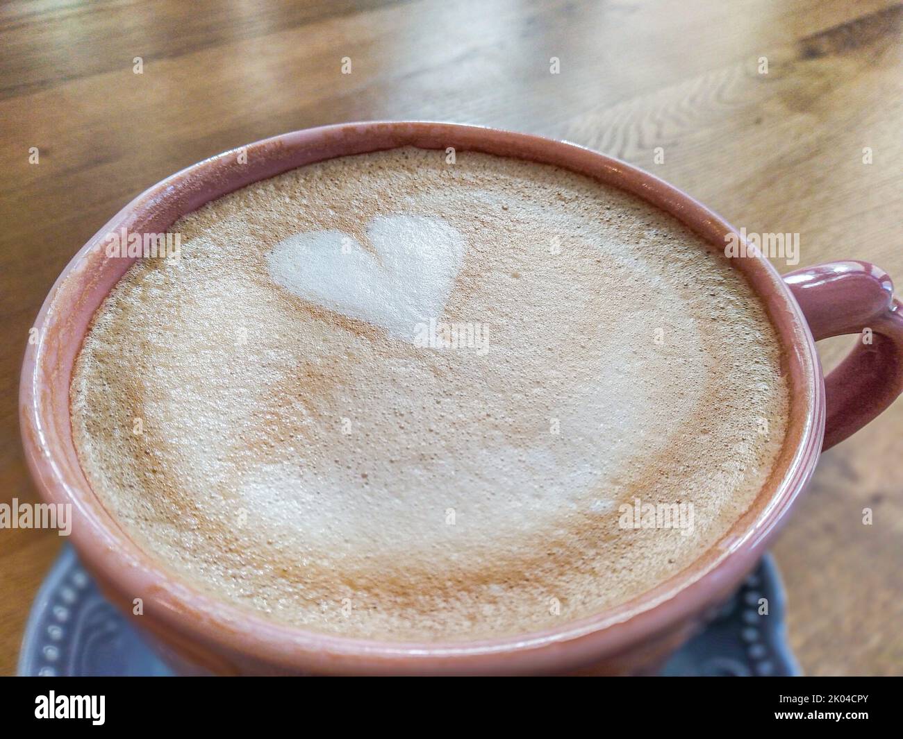 tazza di caffè rosso sul piattino blu con latte a forma di cuore sul tavolo di legno Foto Stock