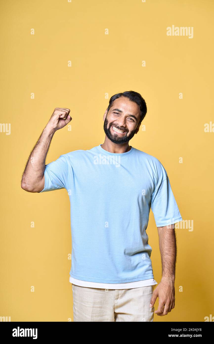 Felice uomo indiano che alza il pugno isolato su sfondo giallo, verticale. Foto Stock