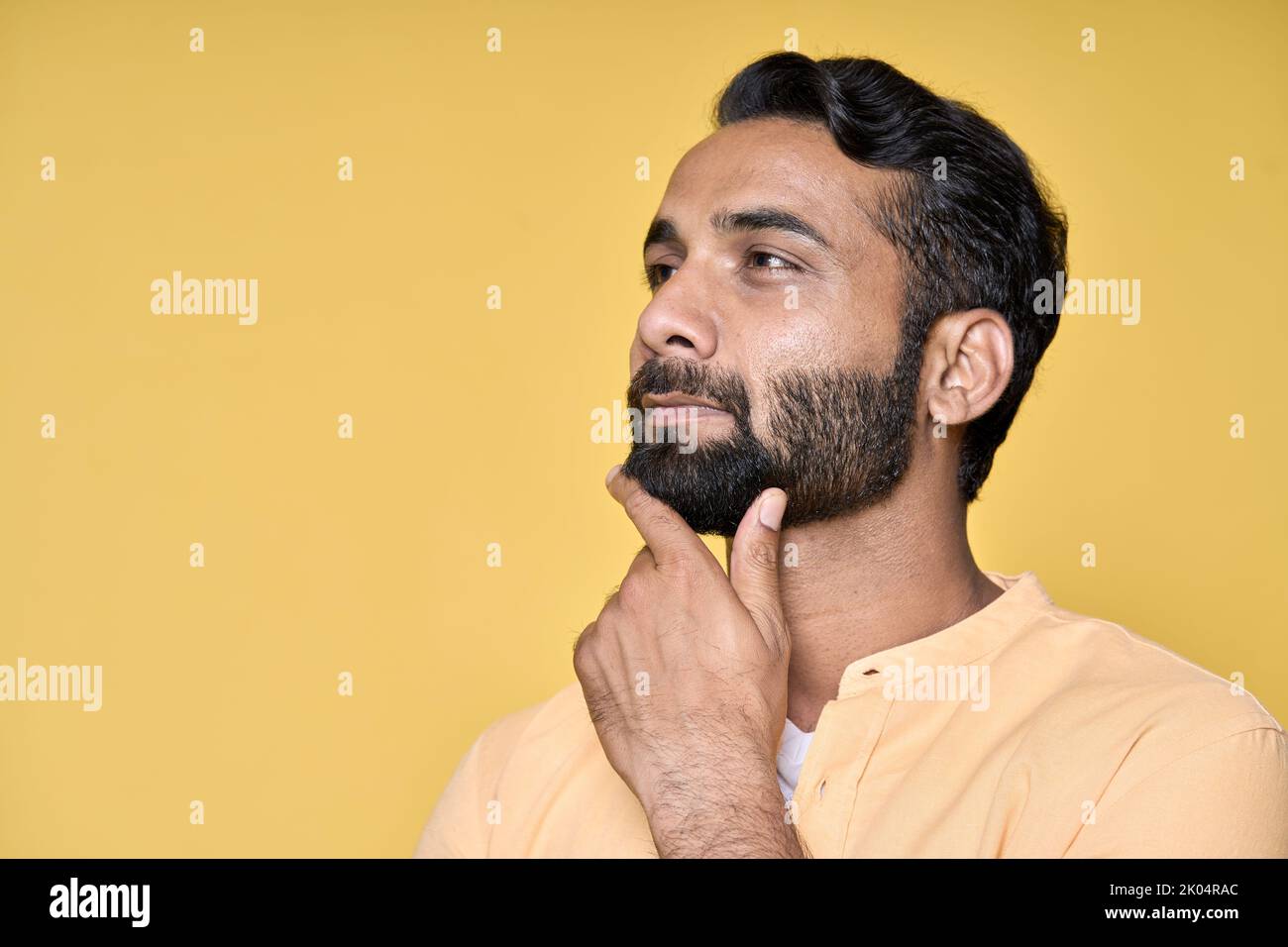 Pensieroso uomo indiano dubbioso pensiero isolato su giallo. Verticale Foto Stock