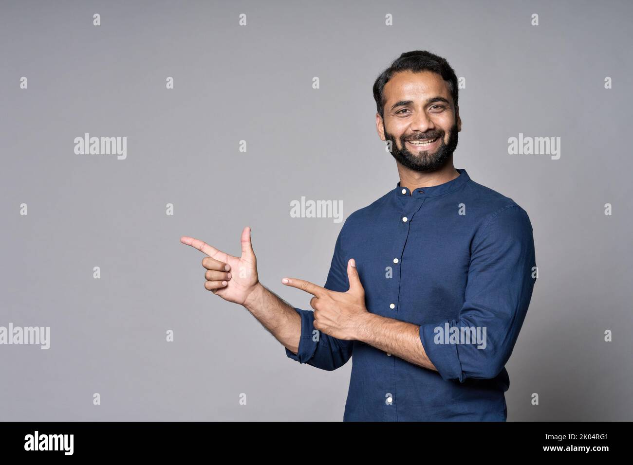Uomo indiano felice di affari che punta le dita che fanno pubblicità isolato sul grigio. Foto Stock