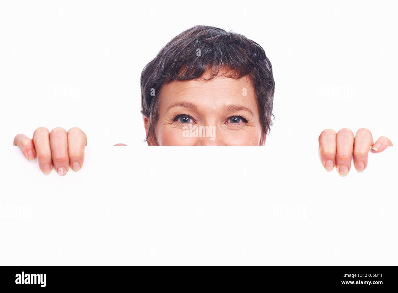 Peekaboo. Primo piano della donna matura di affari che peeking con bordo bianco sopra lo sfondo bianco. Foto Stock