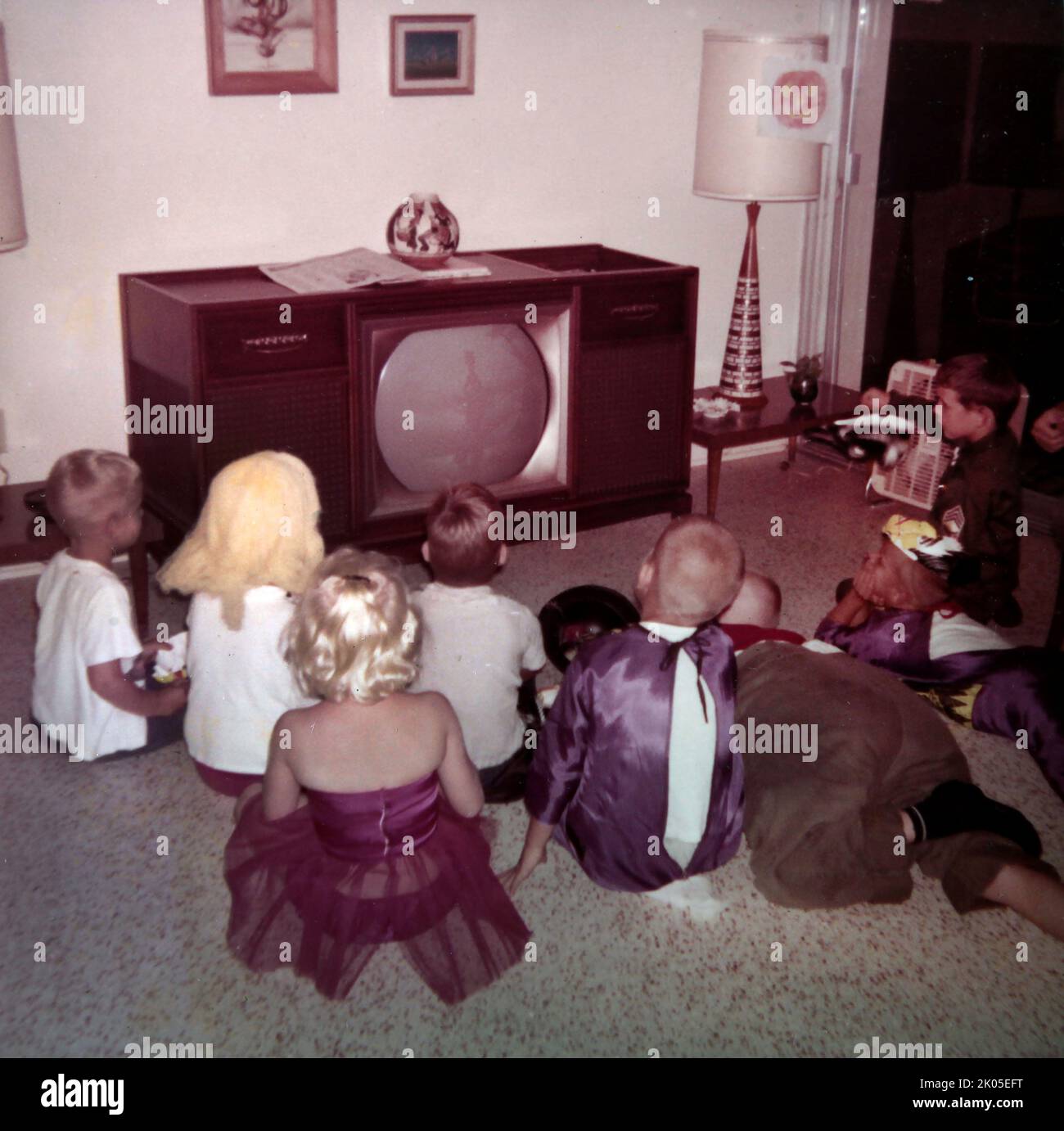 Vista posteriore dei bambini in costume che guardano una televisione alla festa di compleanno, ca. 1960. Foto Stock