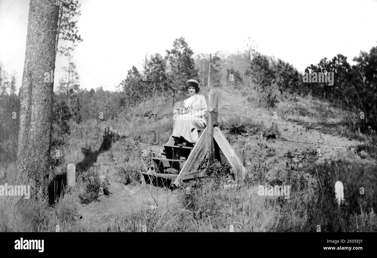 Una donna si siede su un gradino posizionato sopra il filo spinato in un piccolo luogo di sepoltura in Colorado, ca. 1910. Foto Stock