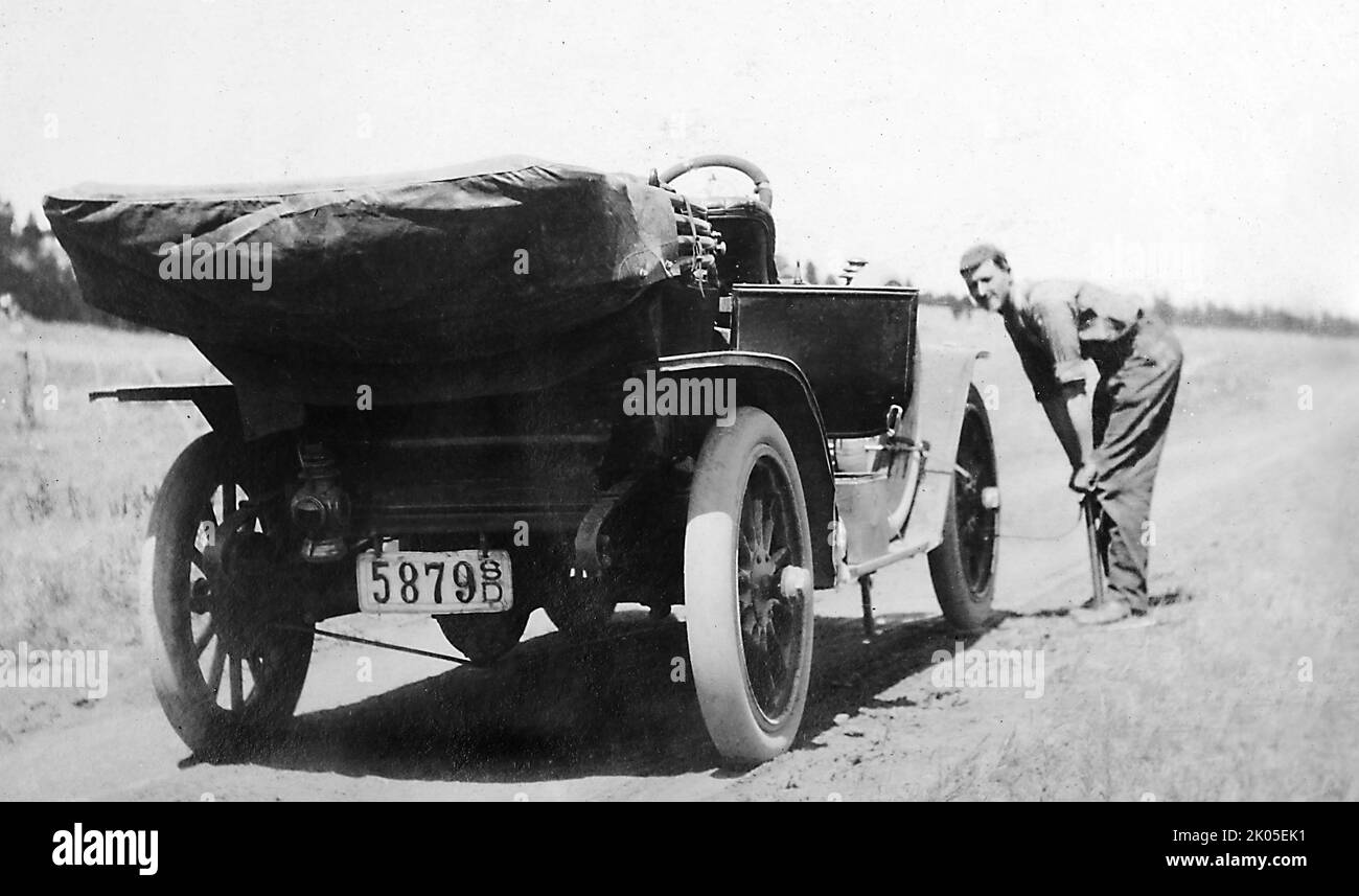 Un giovane uomo riempie il pneumatico della sua auto con una pompa a mano su una strada del South Dakota, ca. 1920 Foto Stock