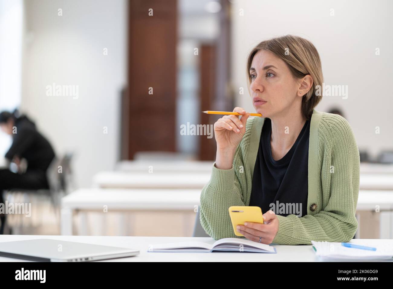 Donna pensiva studente maturo che guarda in lontananza mentre studia in biblioteca, disinteressato nello studio Foto Stock